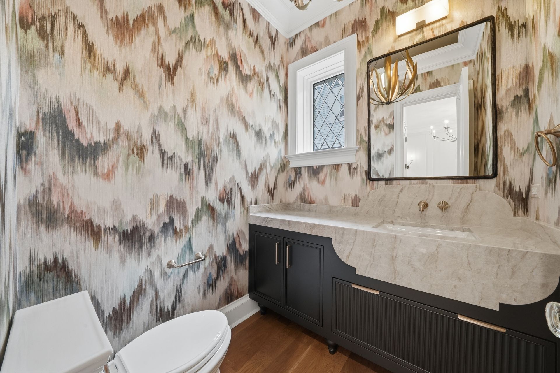 Modern bathroom with patterned wallpaper, black vanity, marble countertop, mirror, and toilet.