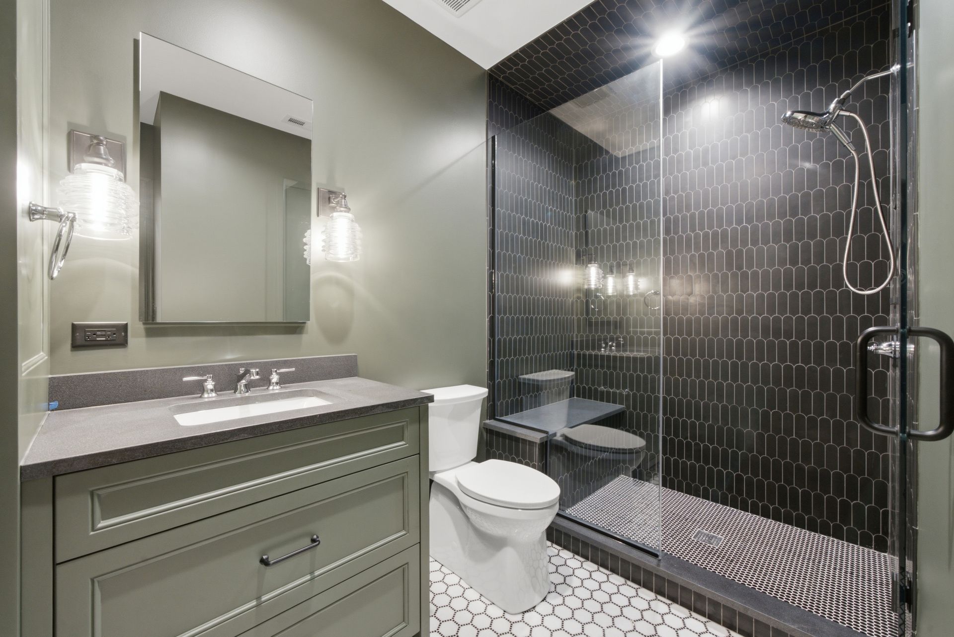 Modern bathroom with gray vanity, mirror, toilet, and black tiled walk-in shower
