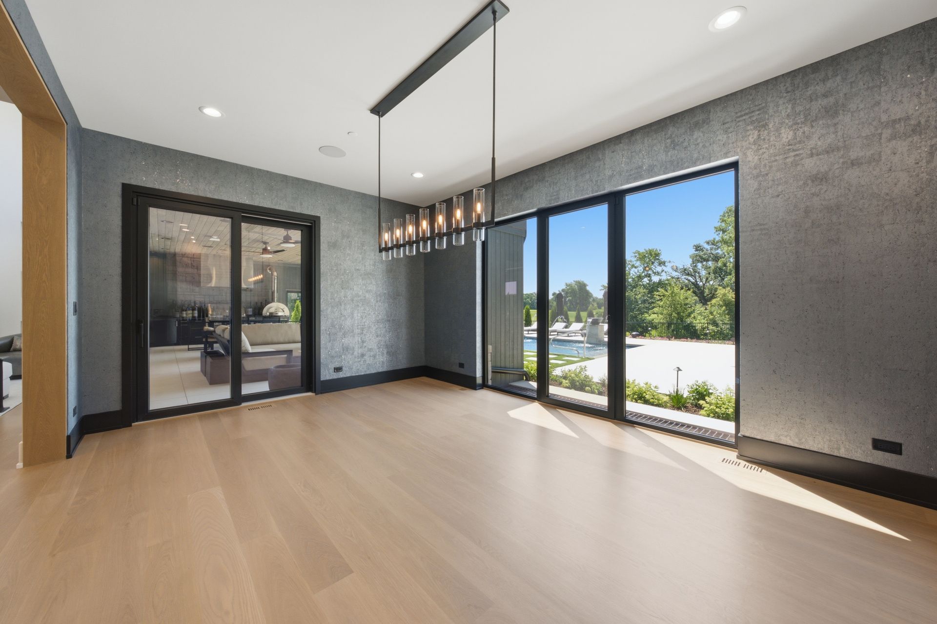 Empty modern living room with dark walls, light wood floors, and large glass doors opening to a patio.