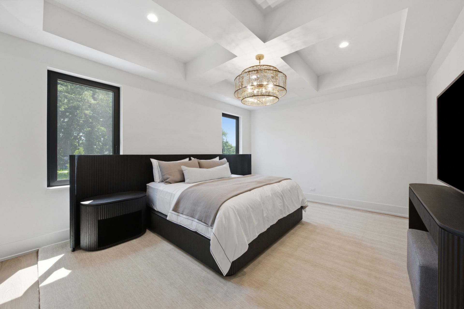 Bright modern bedroom with a black bed frame, white bedding, large windows, and a chandelier