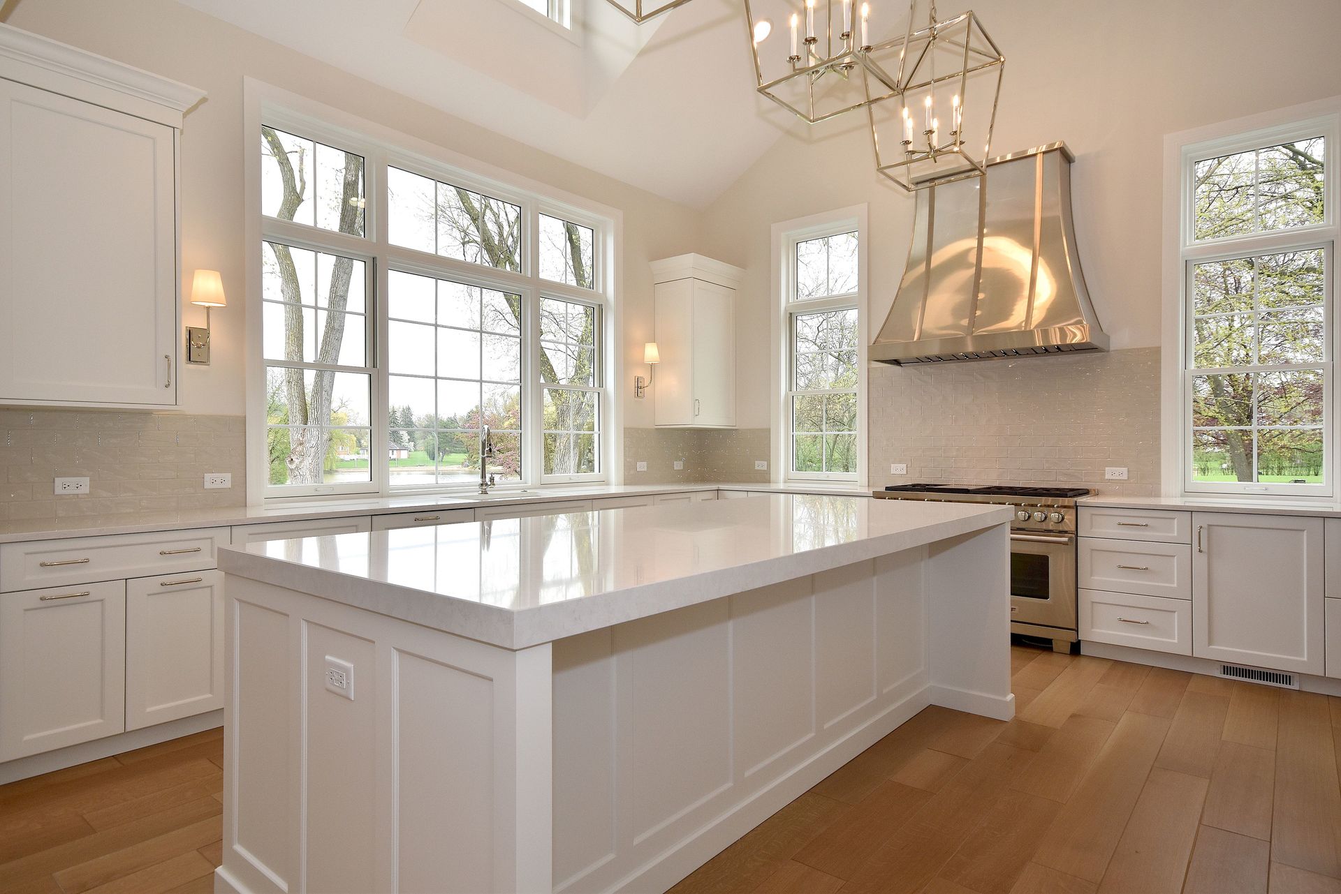 Bright white modern kitchen with a large island, hardwood floors, and tall windows with a chandelier
