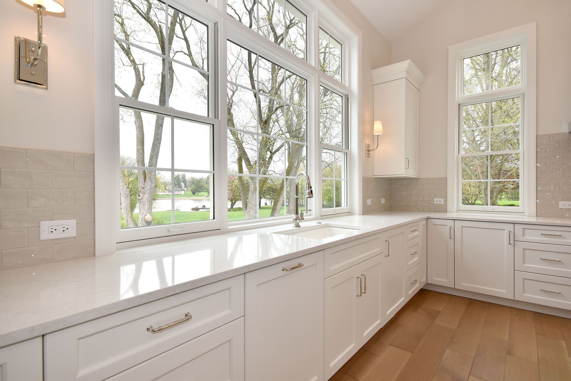 Bright white kitchen with large windows, built-in cabinets, and hardwood floor