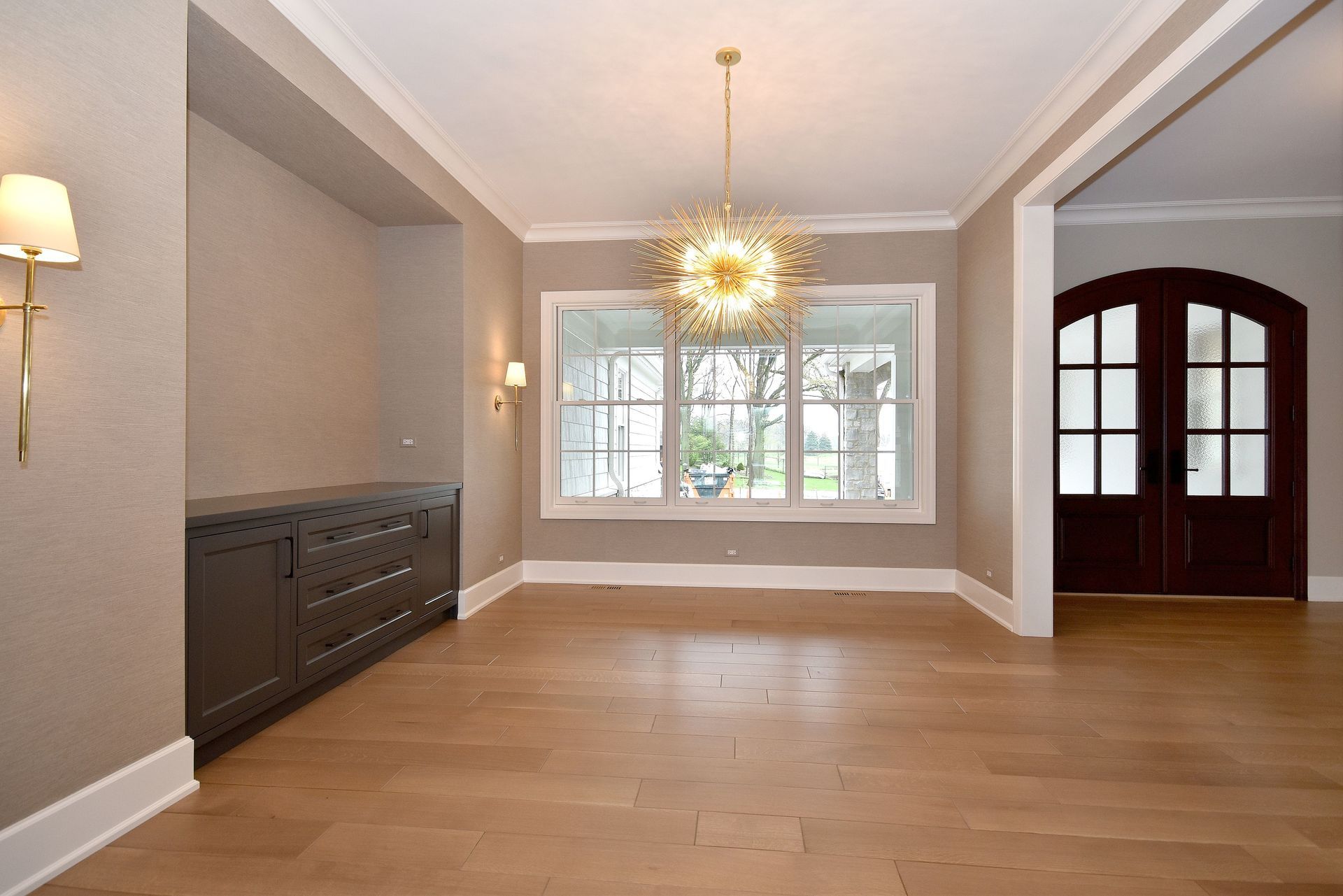 Empty dining room with hardwood floors, gray walls, a window, and a dark arched doorway.