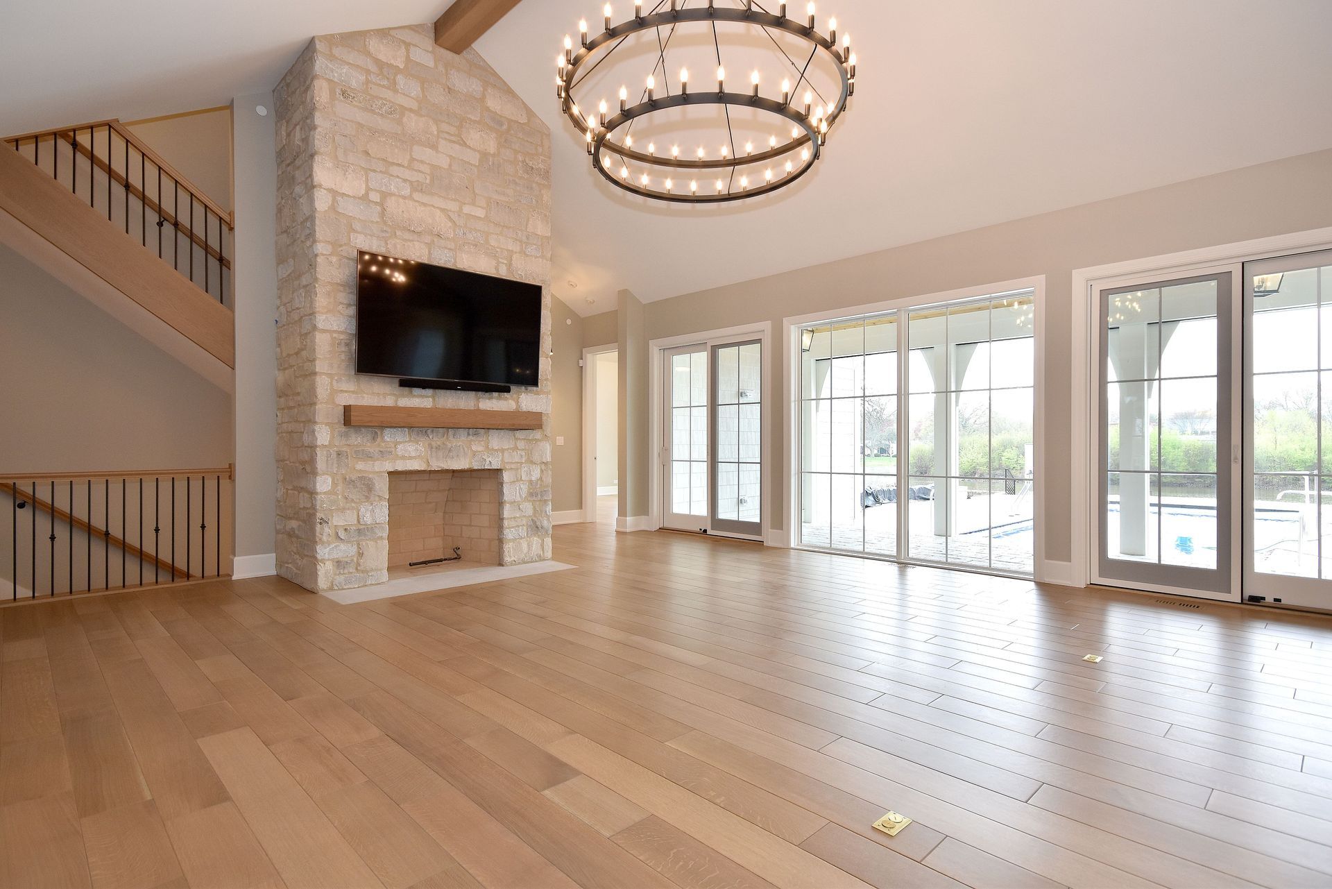 Spacious empty living room with stone fireplace, large windows, hardwood floors, and a chandelier