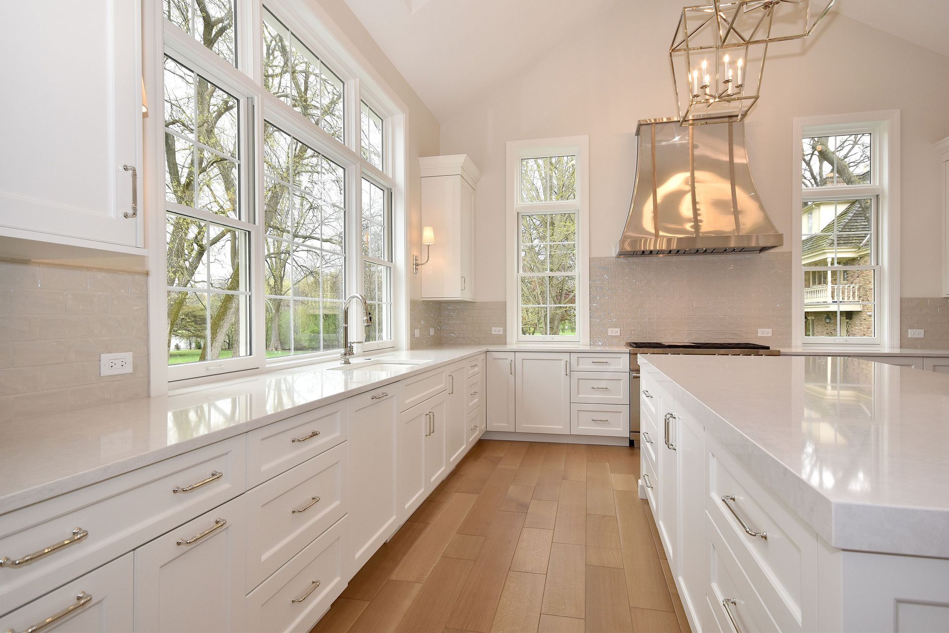 Bright white modern kitchen with large windows, wood floor, and central island range hood