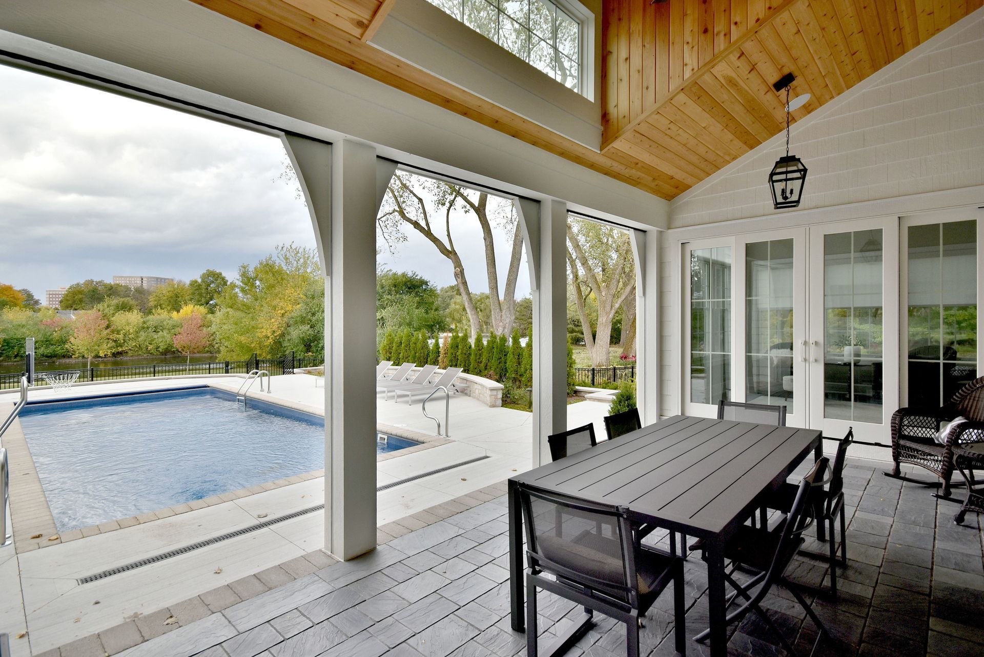 Covered patio with dining table overlooking a backyard pool and lawn