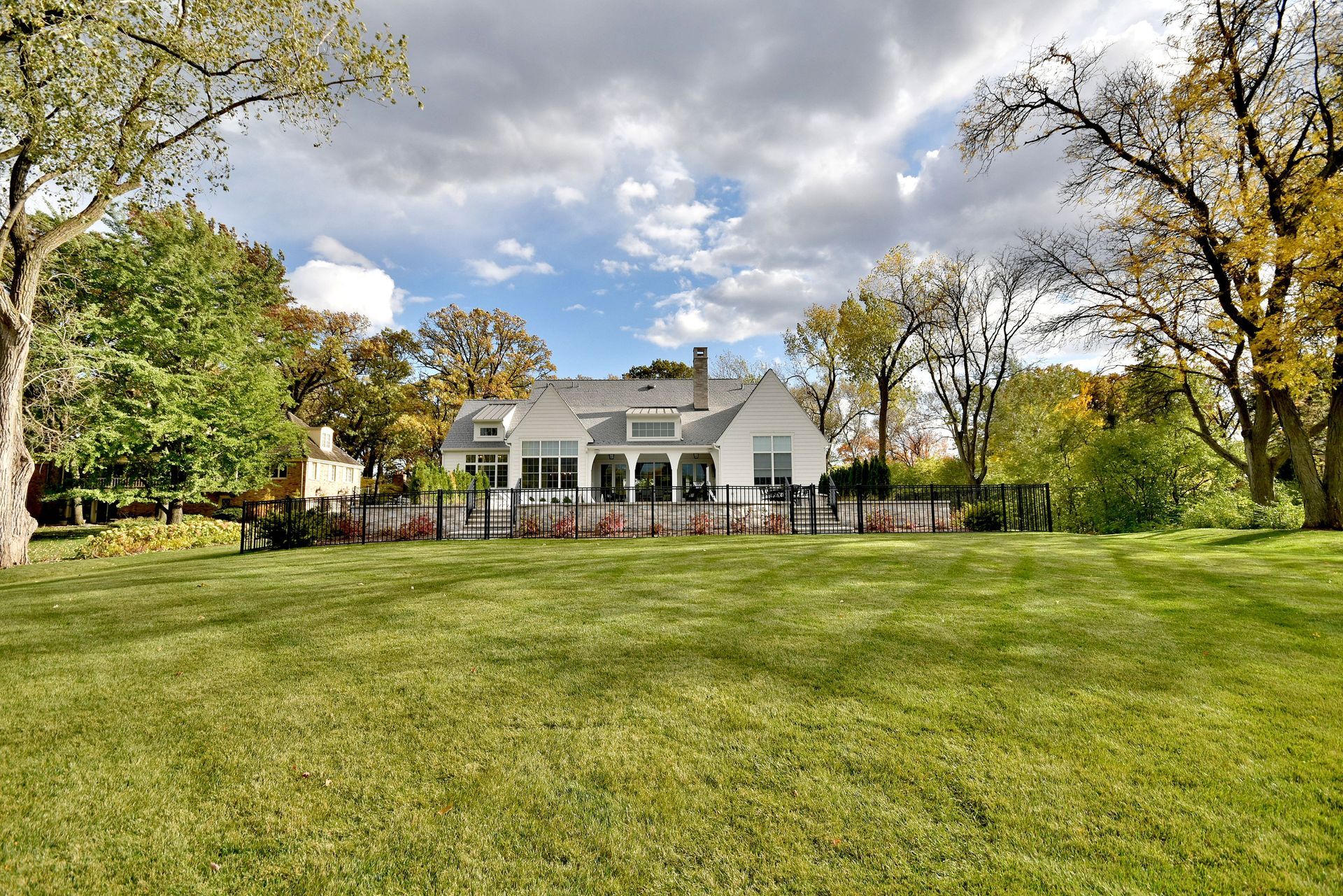 White house with porch and fenced yard on a grassy lawn under cloudy skies