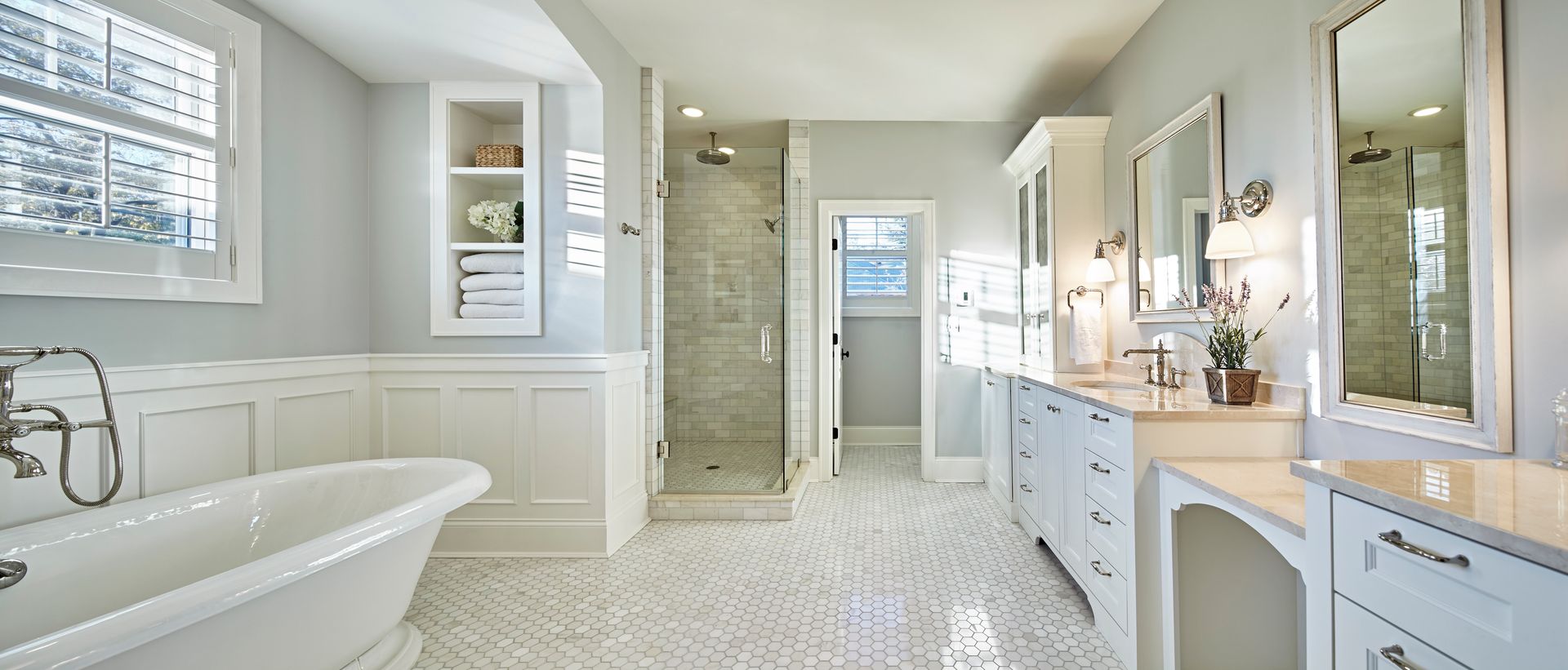 Bright white bathroom with bathtub, double vanity, large mirror, and tiled floor