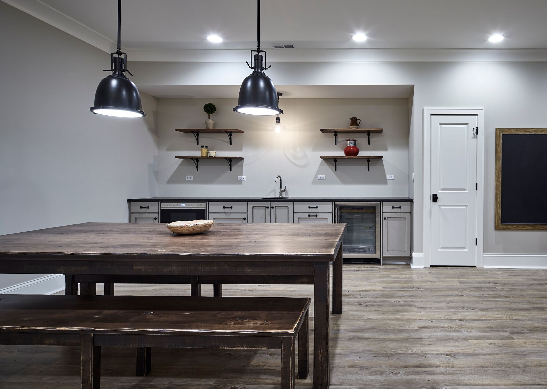 Modern kitchen with large wooden island, pendant lights, white cabinets, and rustic dining table in foreground