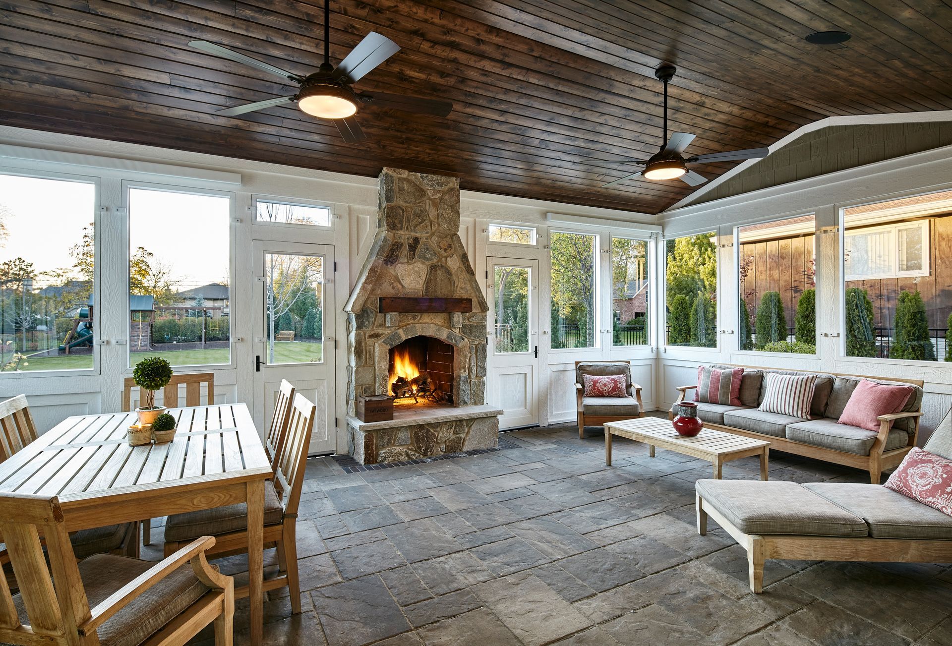 Sunroom with stone fireplace, white dining table, and cushioned seating beside large windows