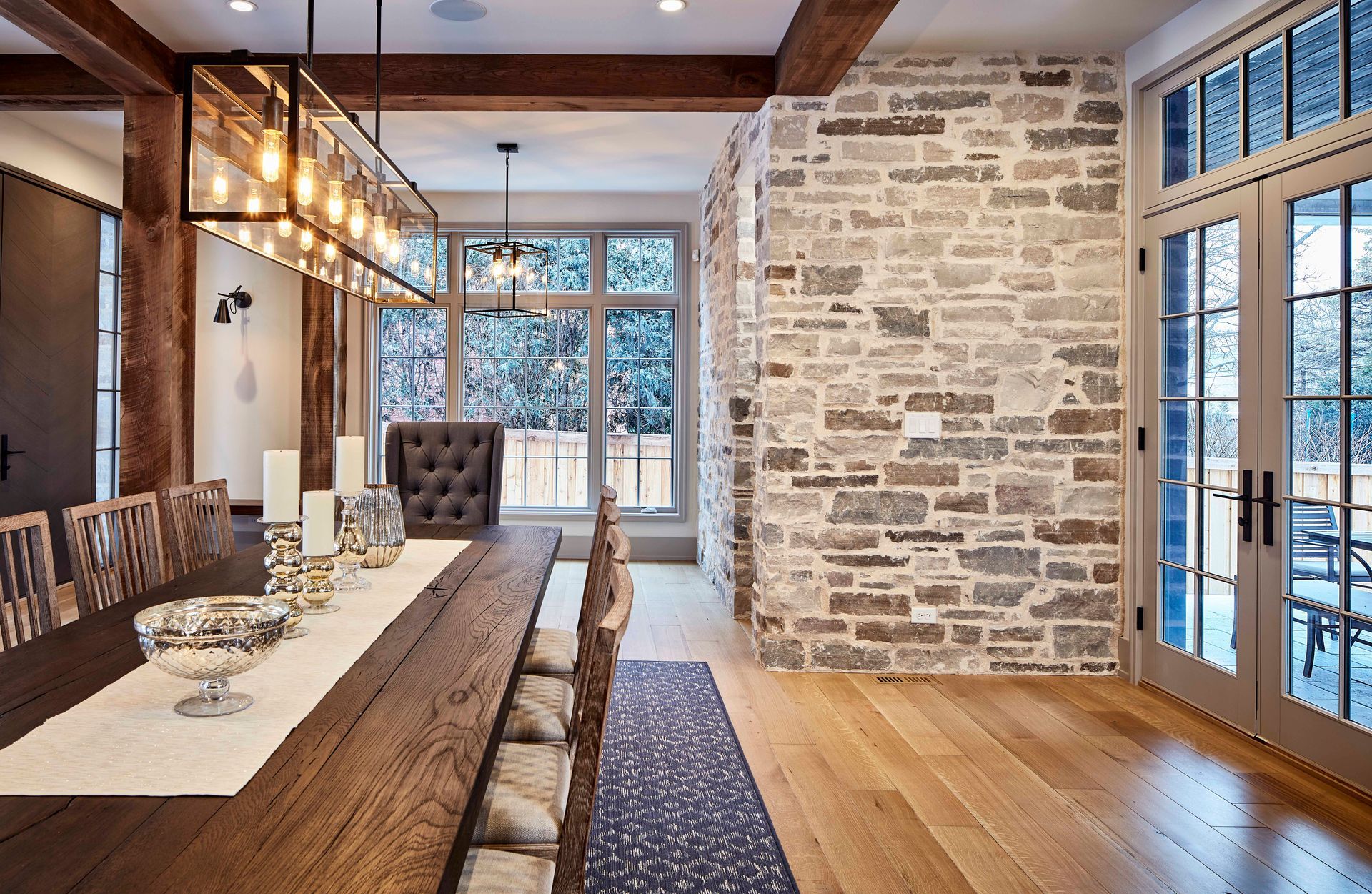 Rustic dining room with stone wall, long wooden table, pendant lights, and large windows