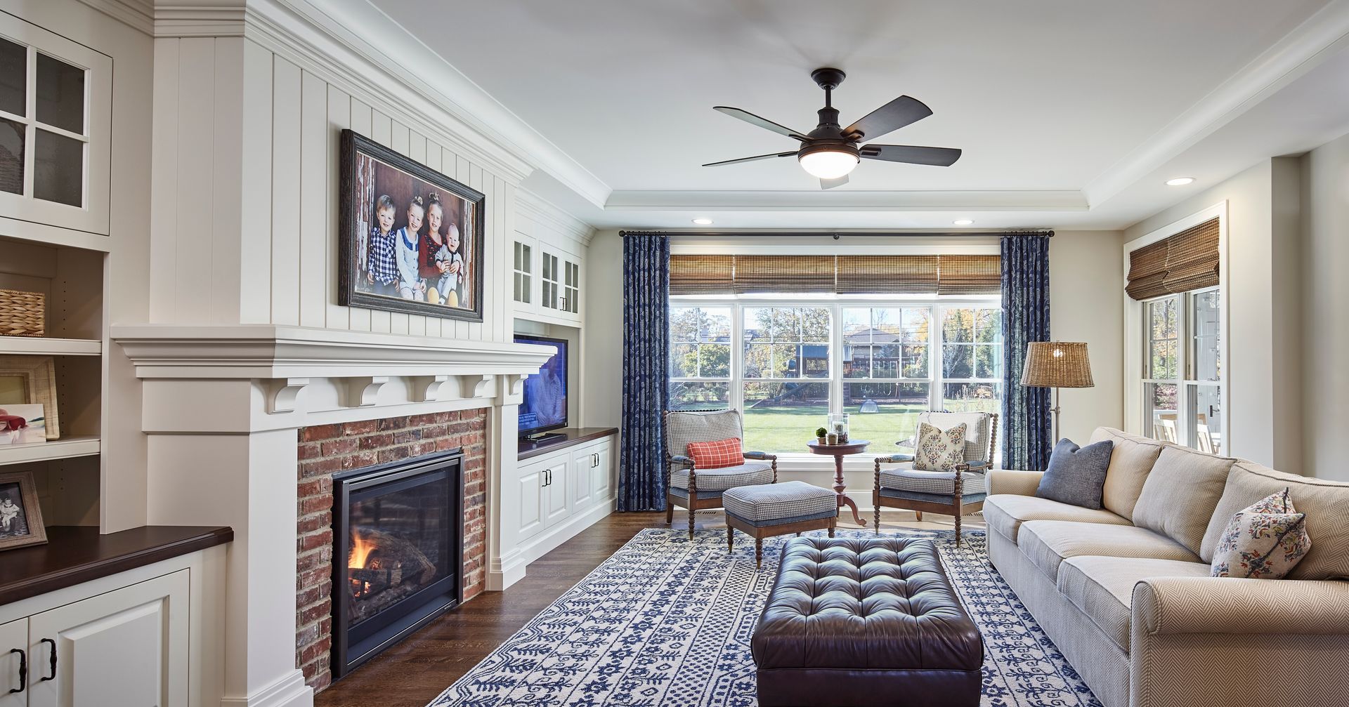 Bright living room with fireplace, sectional sofa, patterned rug, and large window overlooking a backyard.