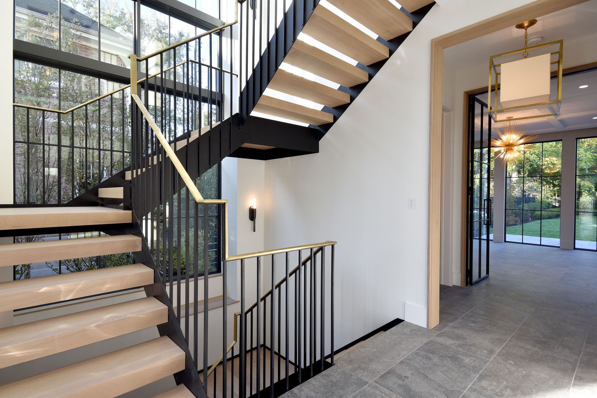 Modern interior staircase with black railings, white walls, and a hallway leading to glass doors
