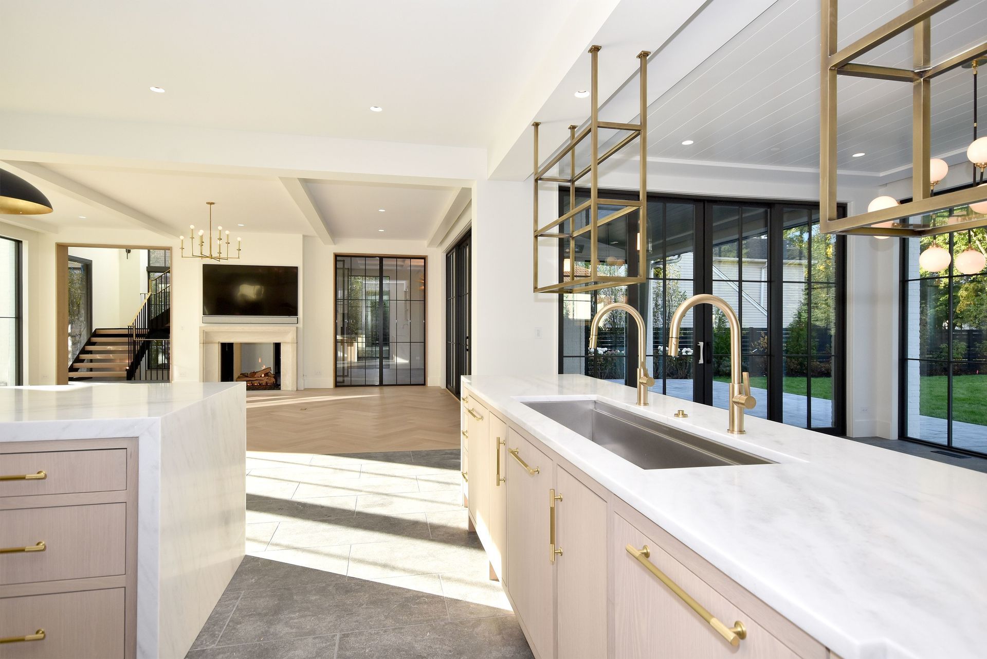 Bright modern kitchen with marble island, gold fixtures, and floor-to-ceiling glass doors overlooking a patio
