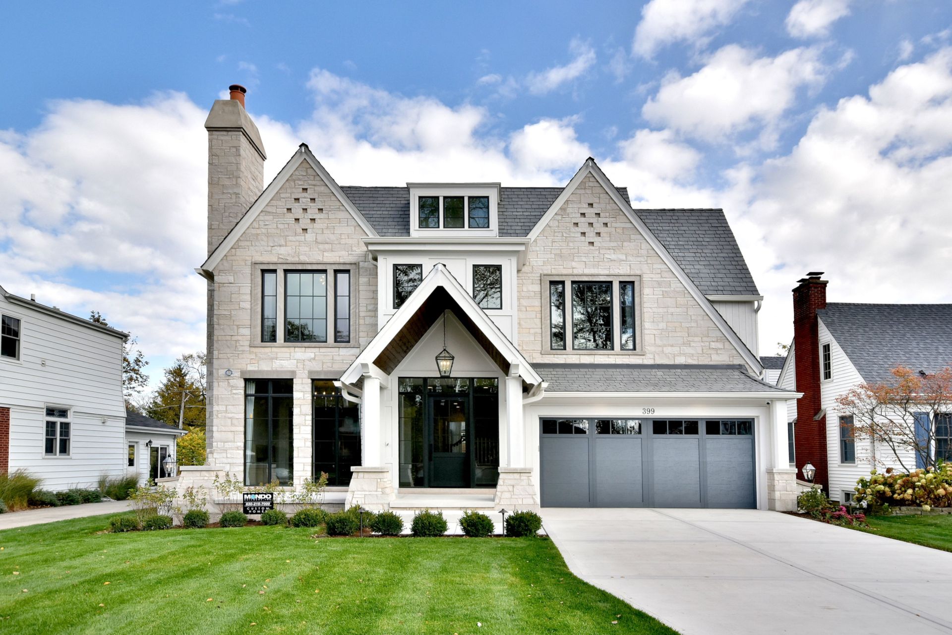 Modern gray two-story house with gabled roof, front porch, and attached double garage on a landscaped lawn