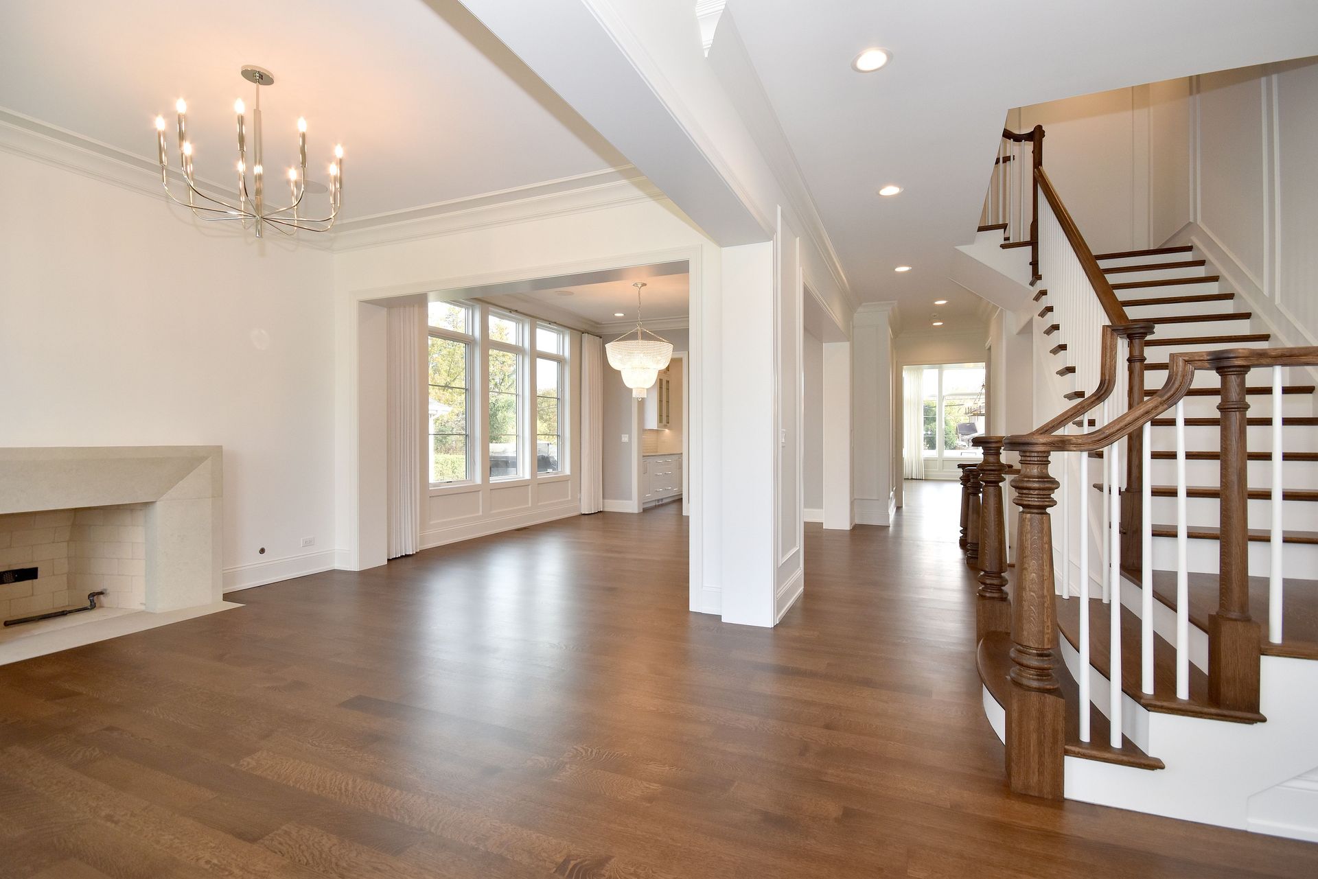 Spacious empty living room with hardwood floors, chandeliers, fireplace, and curved staircase