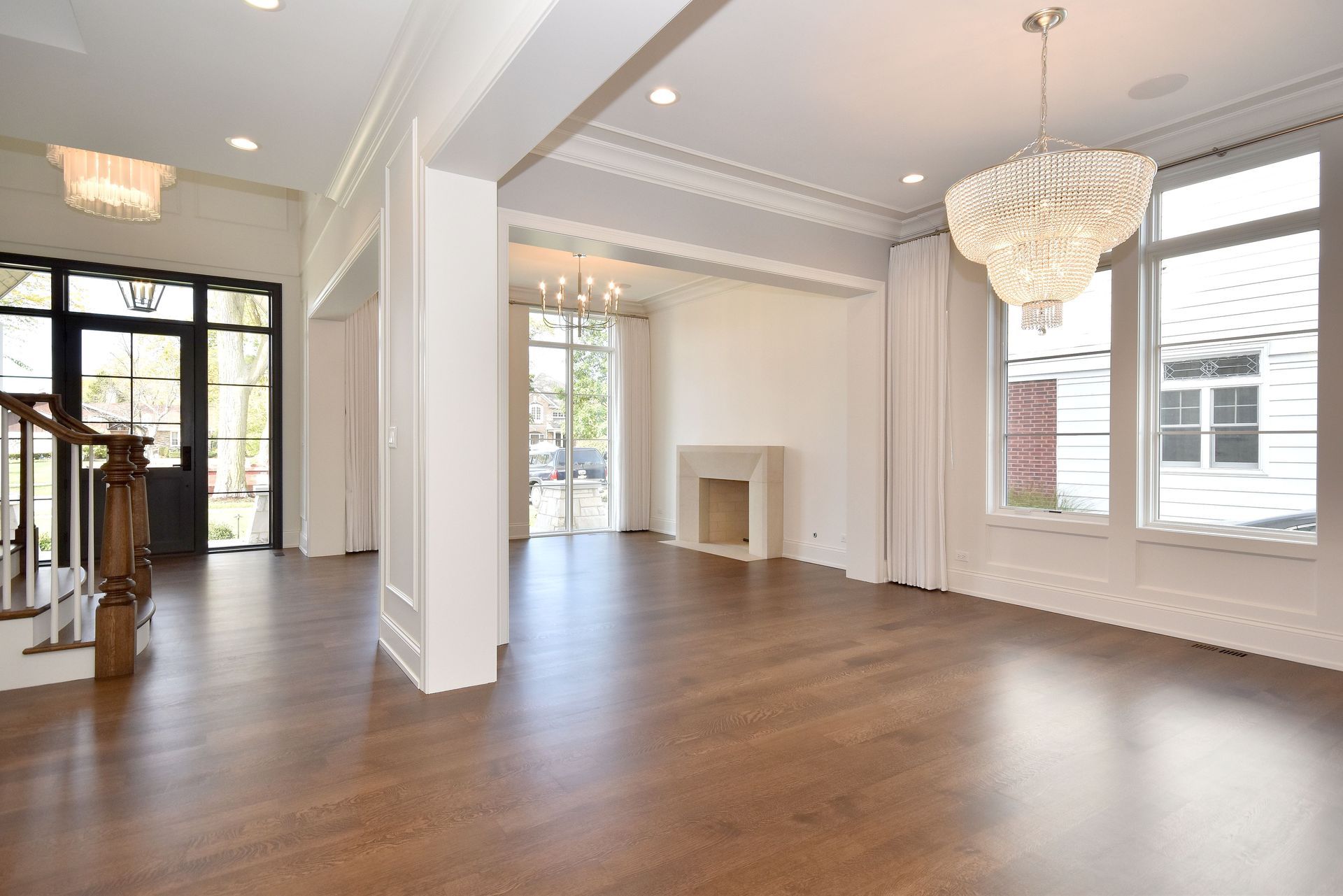 Bright, empty living room with hardwood floors, white walls, large windows, and a chandelier
