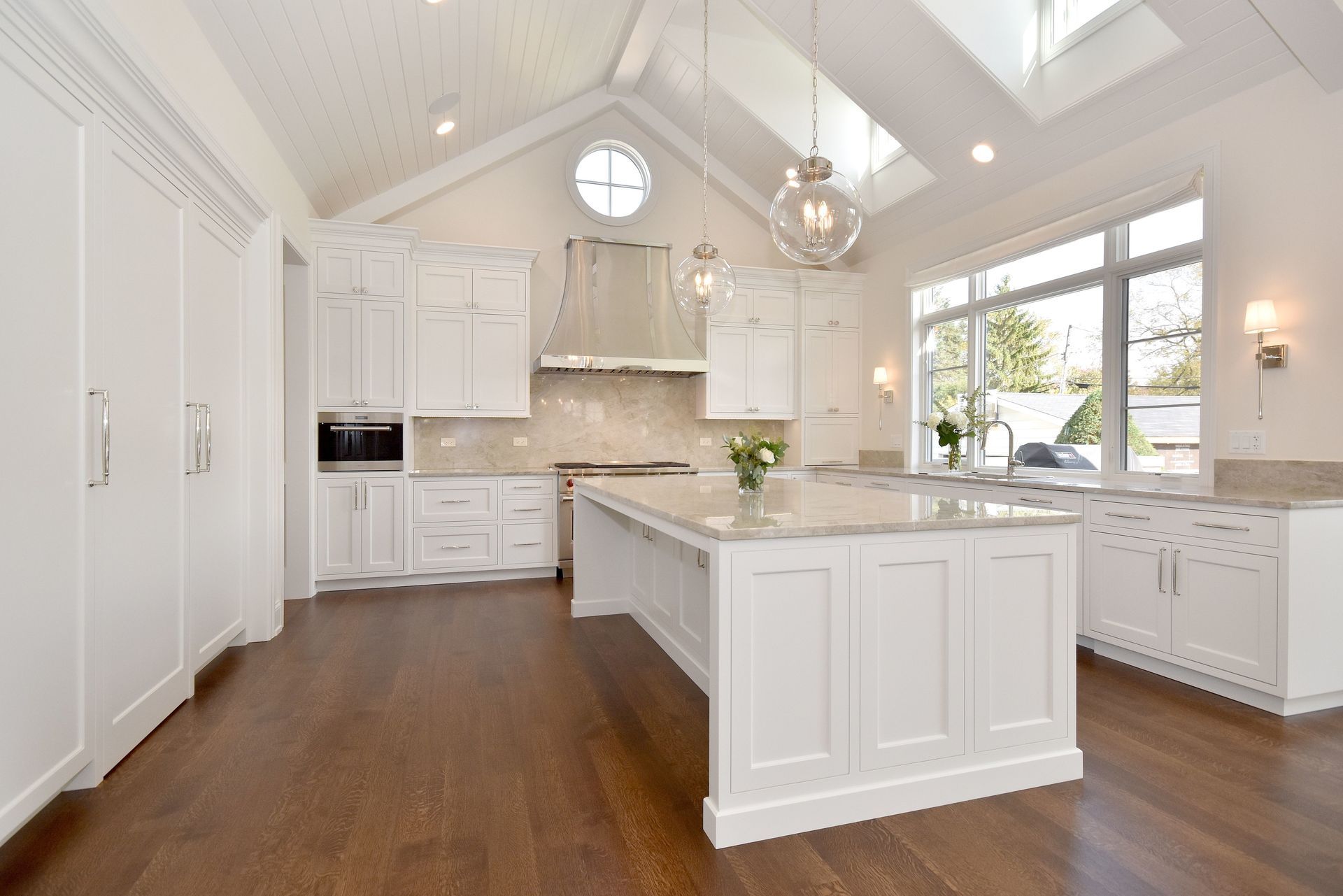 Bright white kitchen with island, hardwood floors, skylights, and large windows overlooking greenery