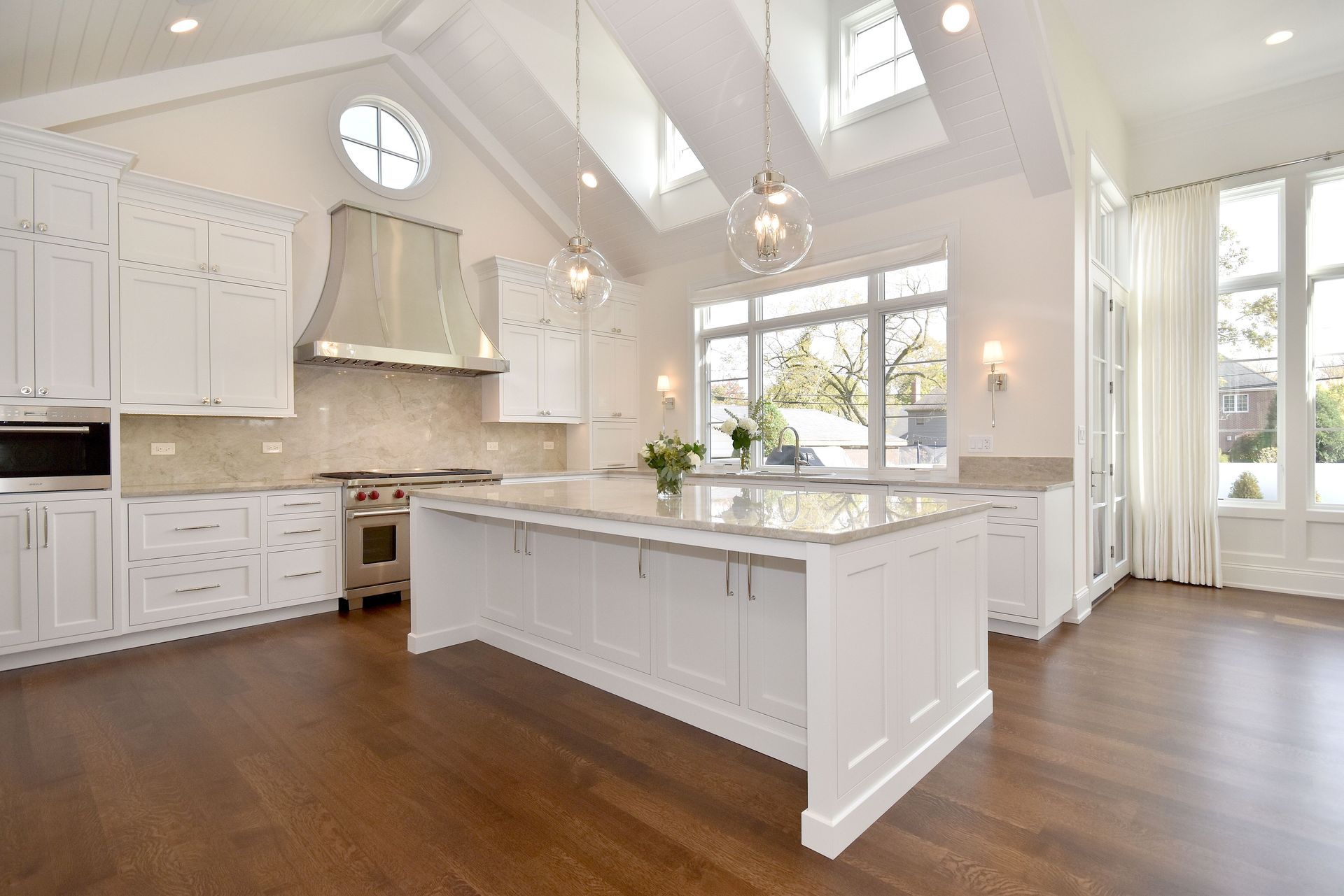 Bright white kitchen with island, hardwood floors, large windows, and vaulted ceiling with skylights