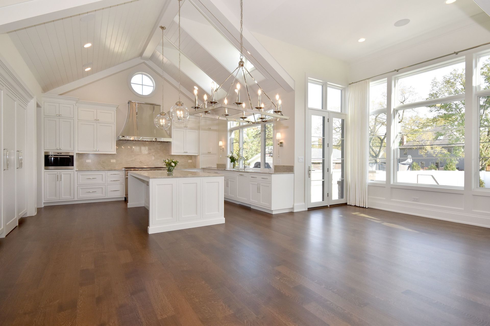 Bright white kitchen with vaulted ceiling, island, wood floors, and large windows