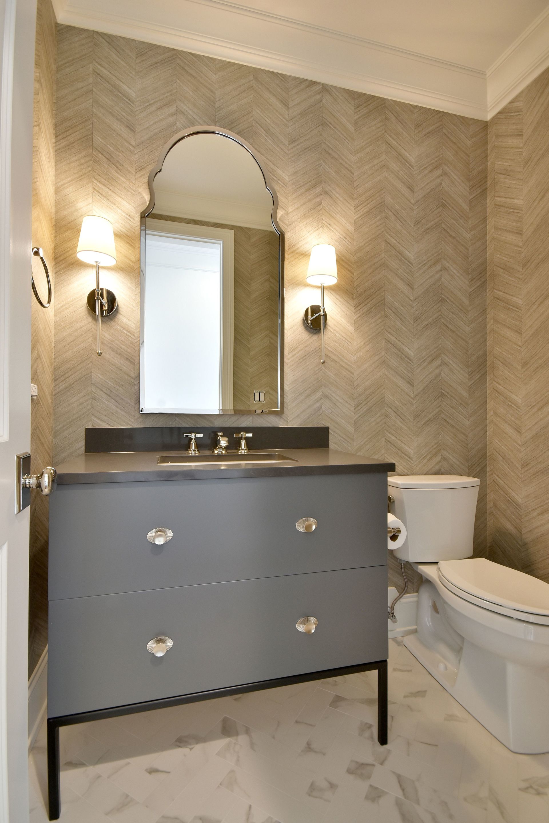 Elegant bathroom with gray vanity, arched mirror, wall sconces, and toilet on the right