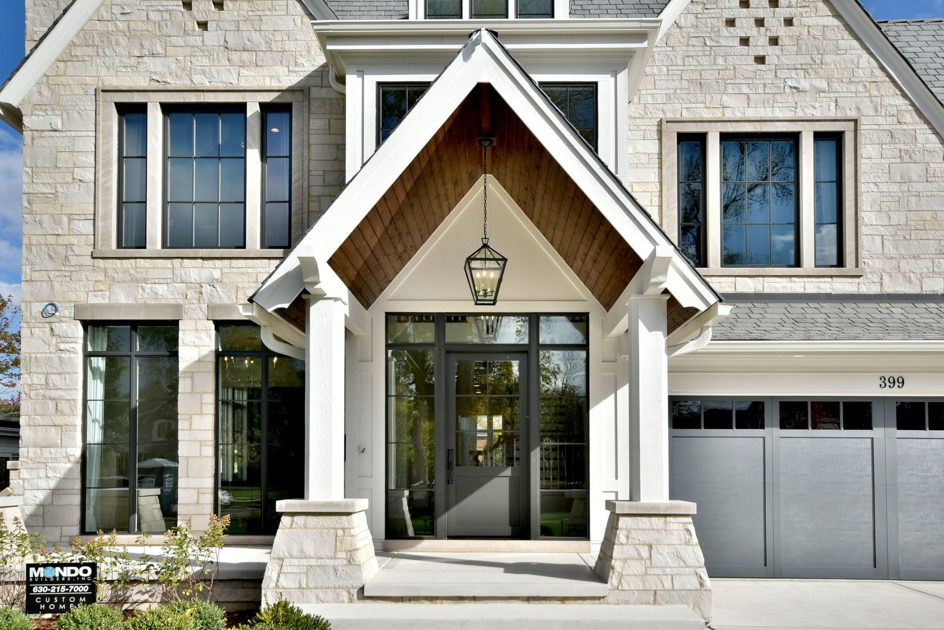 Stone house front entrance with peaked porch, glass doors, and two garage doors on the right