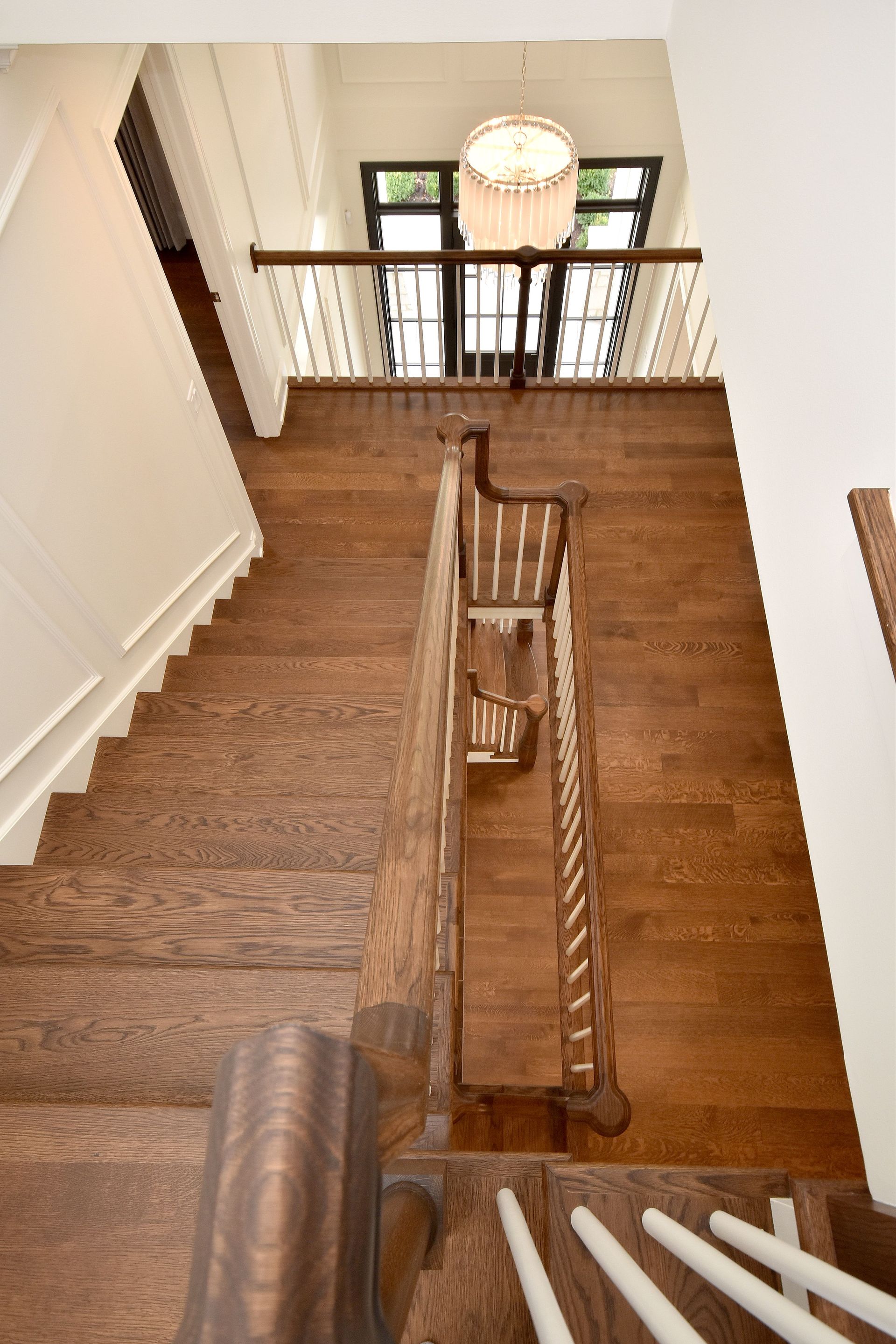 Staircase with brown carpet, wooden railing, and a hanging light above a foyer.