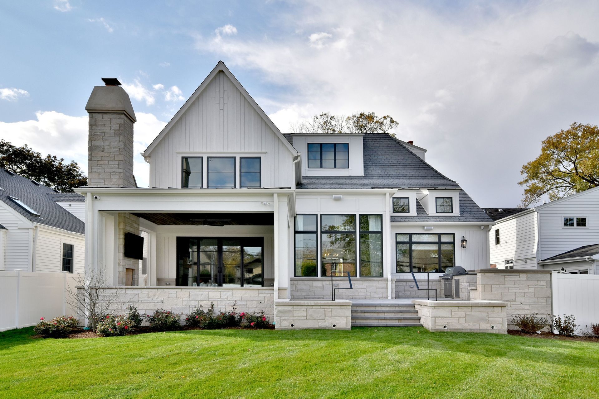 White modern house with gray roof, large windows, front porch, and green lawn under a cloudy sky