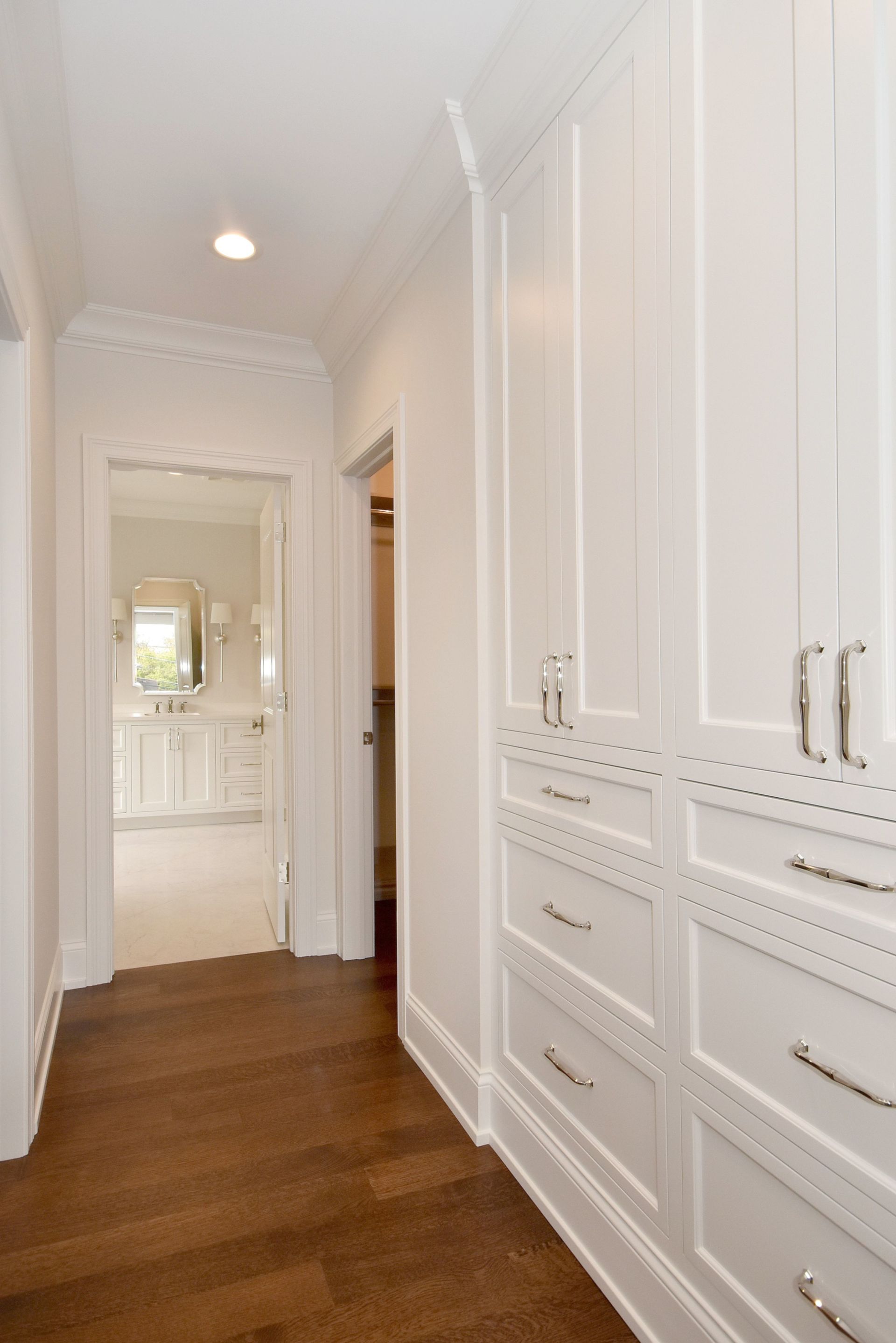 Bright white hallway with built-in cabinets and drawers, wood floor, and a mirror at the far end.