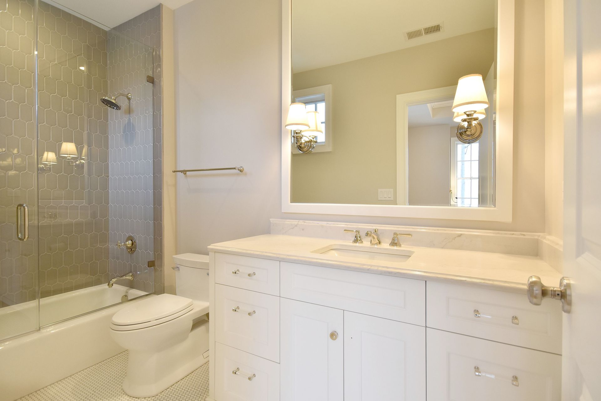 Bright bathroom with white vanity, large mirror, and tiled bathtub/shower area