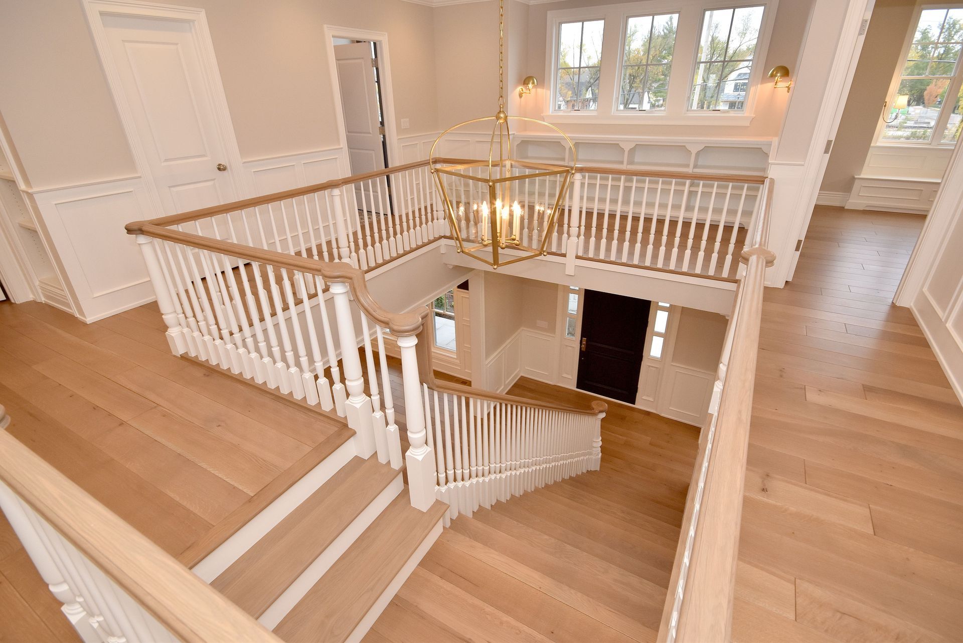 Bright foyer with wood stairs, white railings, and open upper landing overlooking a lower level.
