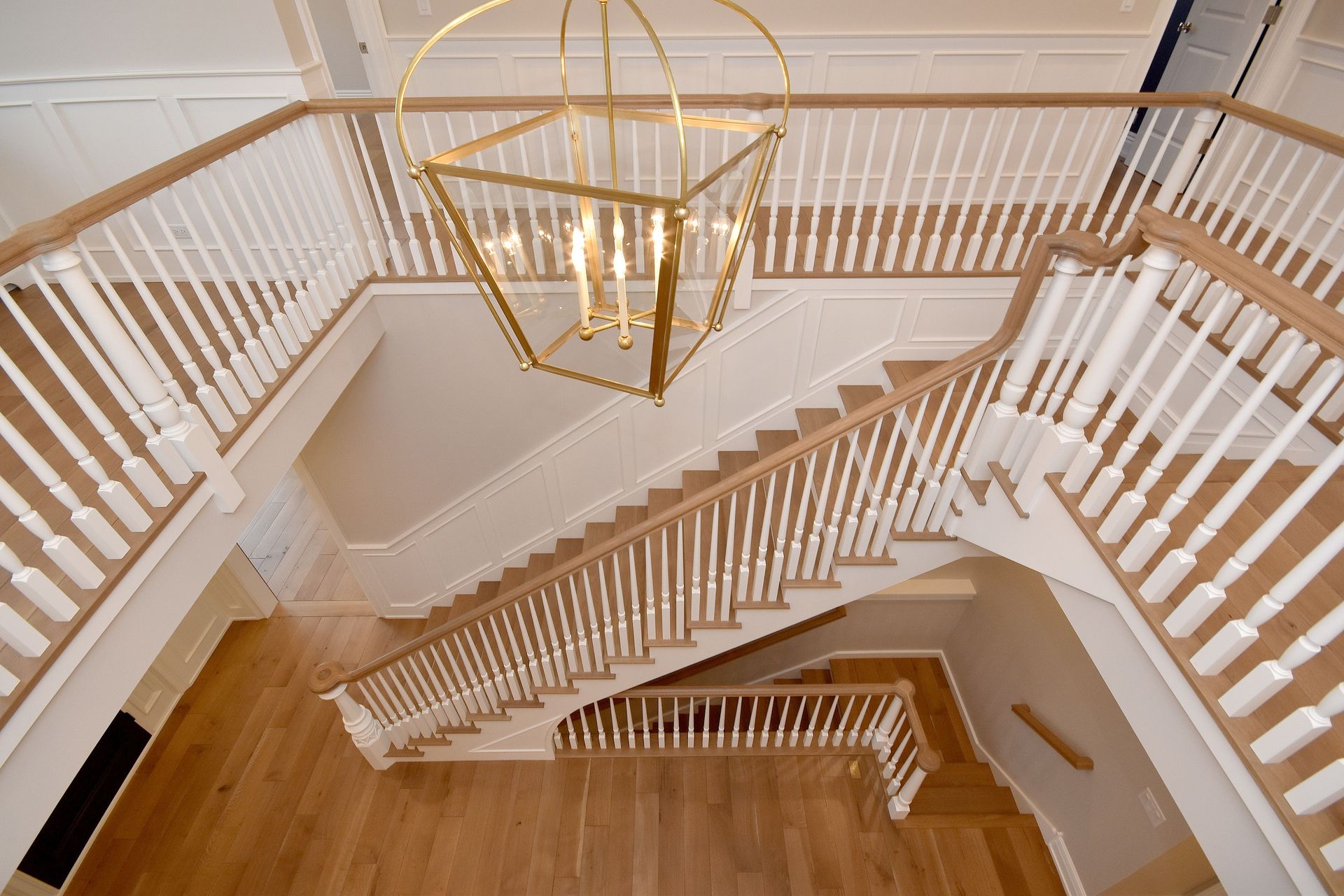 Elegant white staircase with gold railings and a chandelier in a bright interior foyer