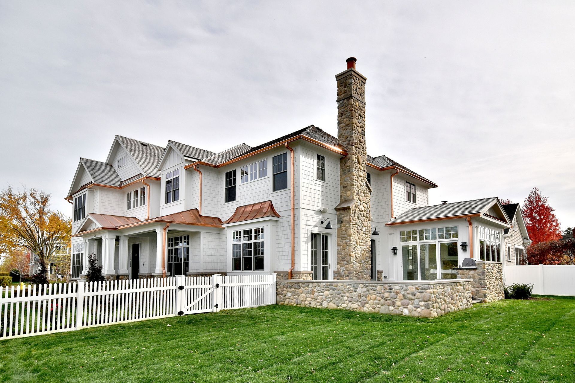 Large white two-story house with red roof, stone chimney, and white fence on a green lawn