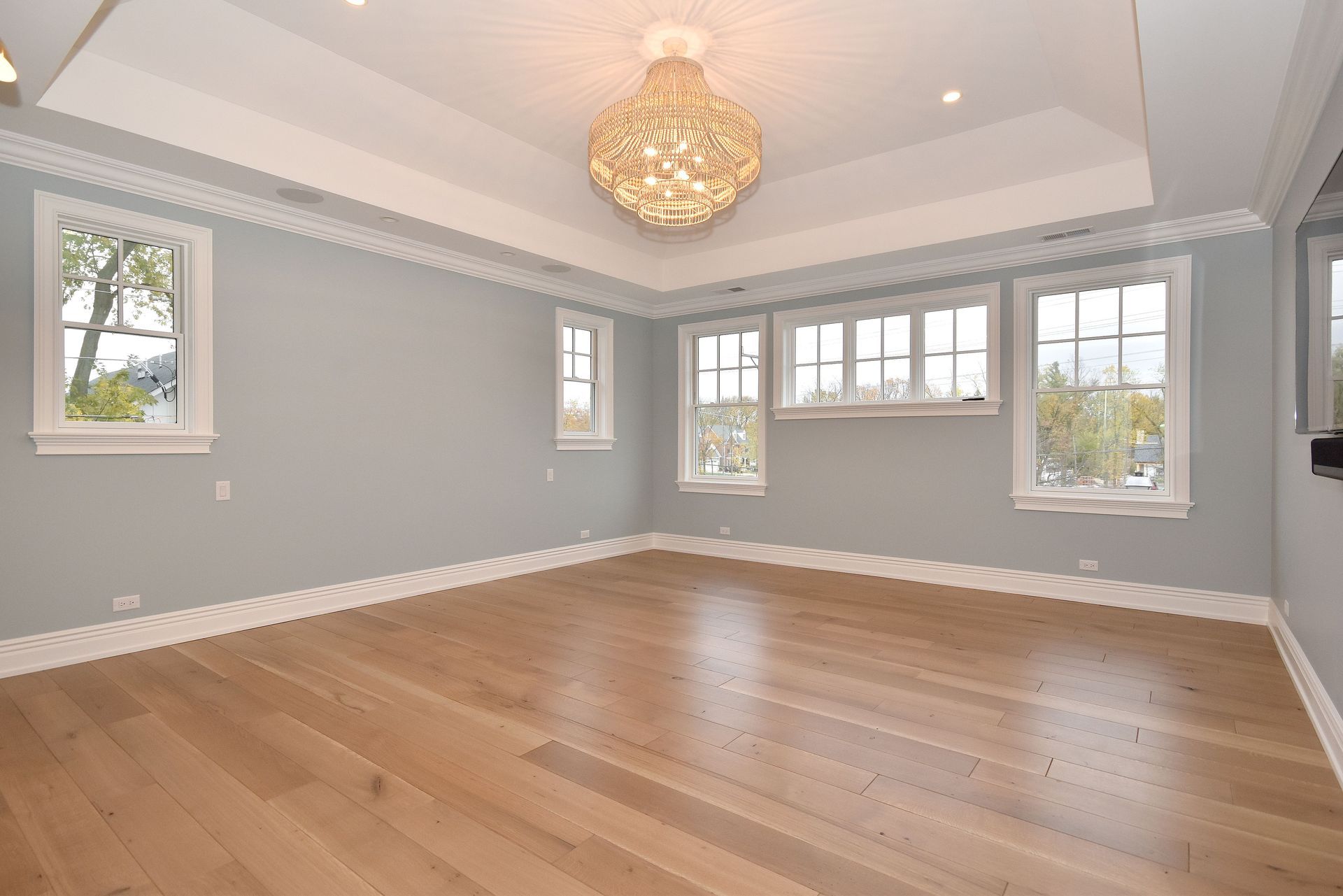 Empty modern living room with gray walls, hardwood floors, white trim, and a chandelier