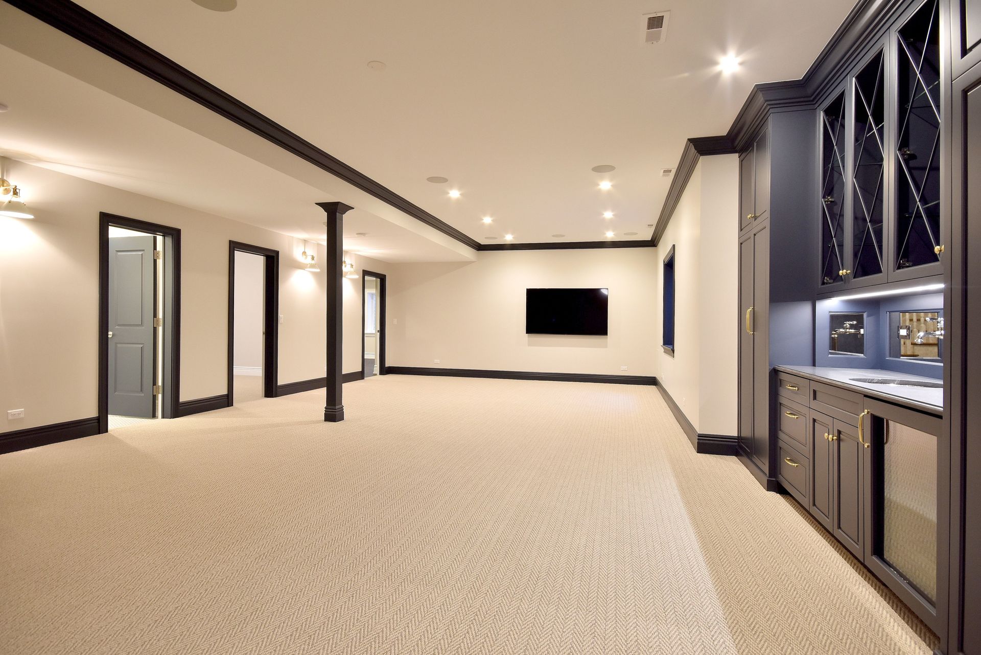 Spacious modern media room with beige carpet, recessed lights, wall-mounted TV, and built-in cabinets