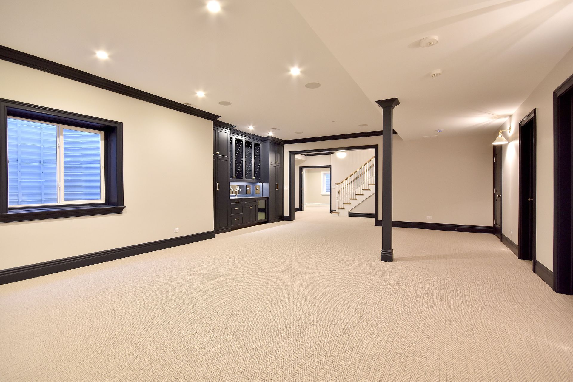 Spacious empty basement with beige carpet, white walls, recessed lights, and a black support column