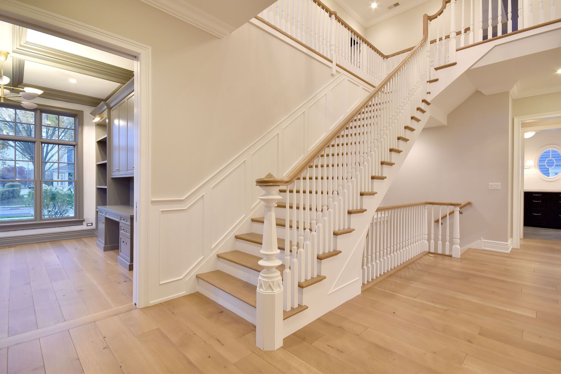 Bright foyer with white staircase, hardwood floors, and open living spaces.