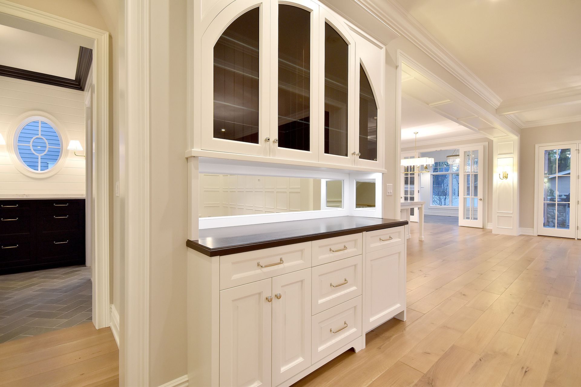 Bright modern kitchen with white cabinets, black countertops, and light wood floors leading to a hallway.