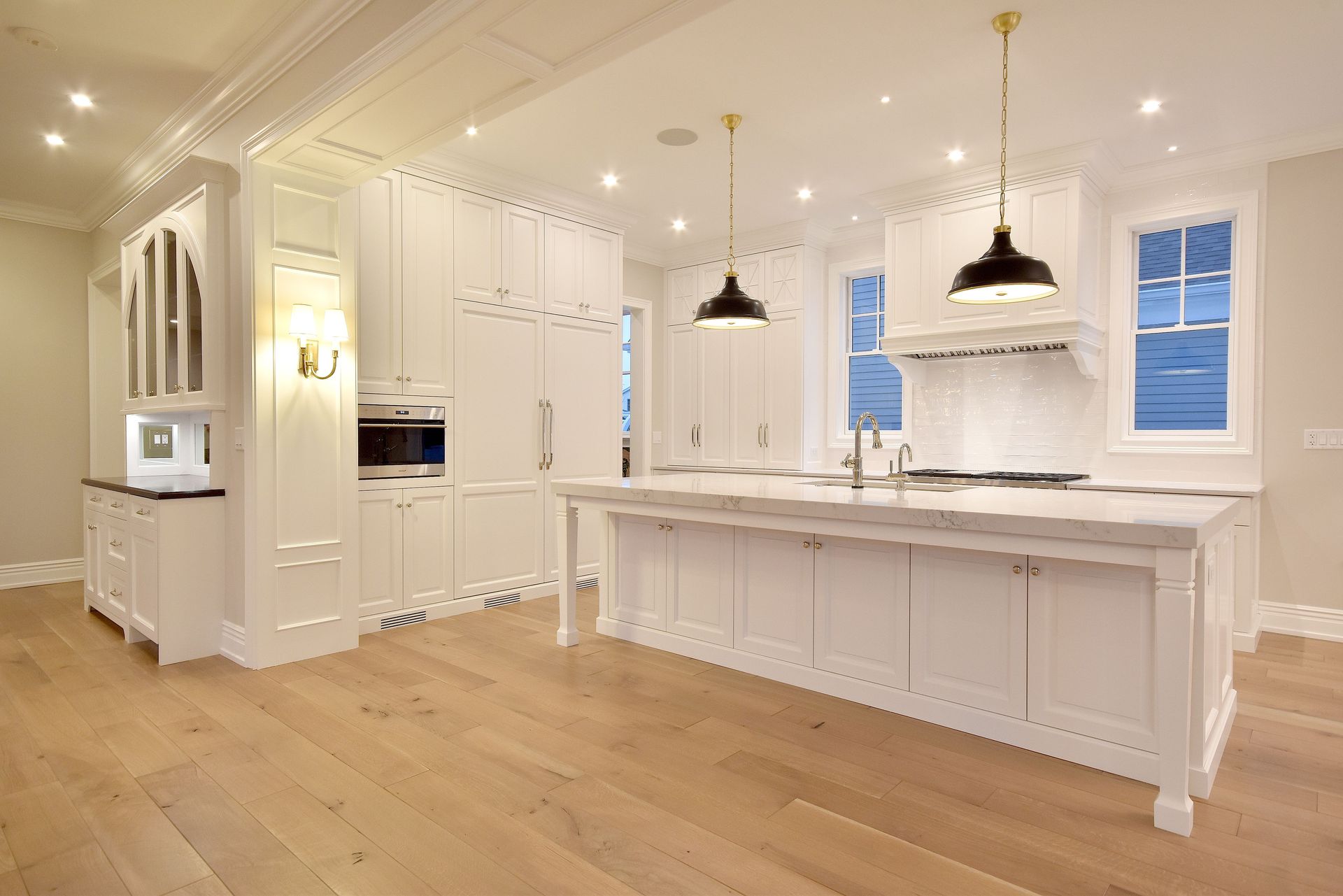 Bright white modern kitchen with marble island, pendant lights, and light wood floors