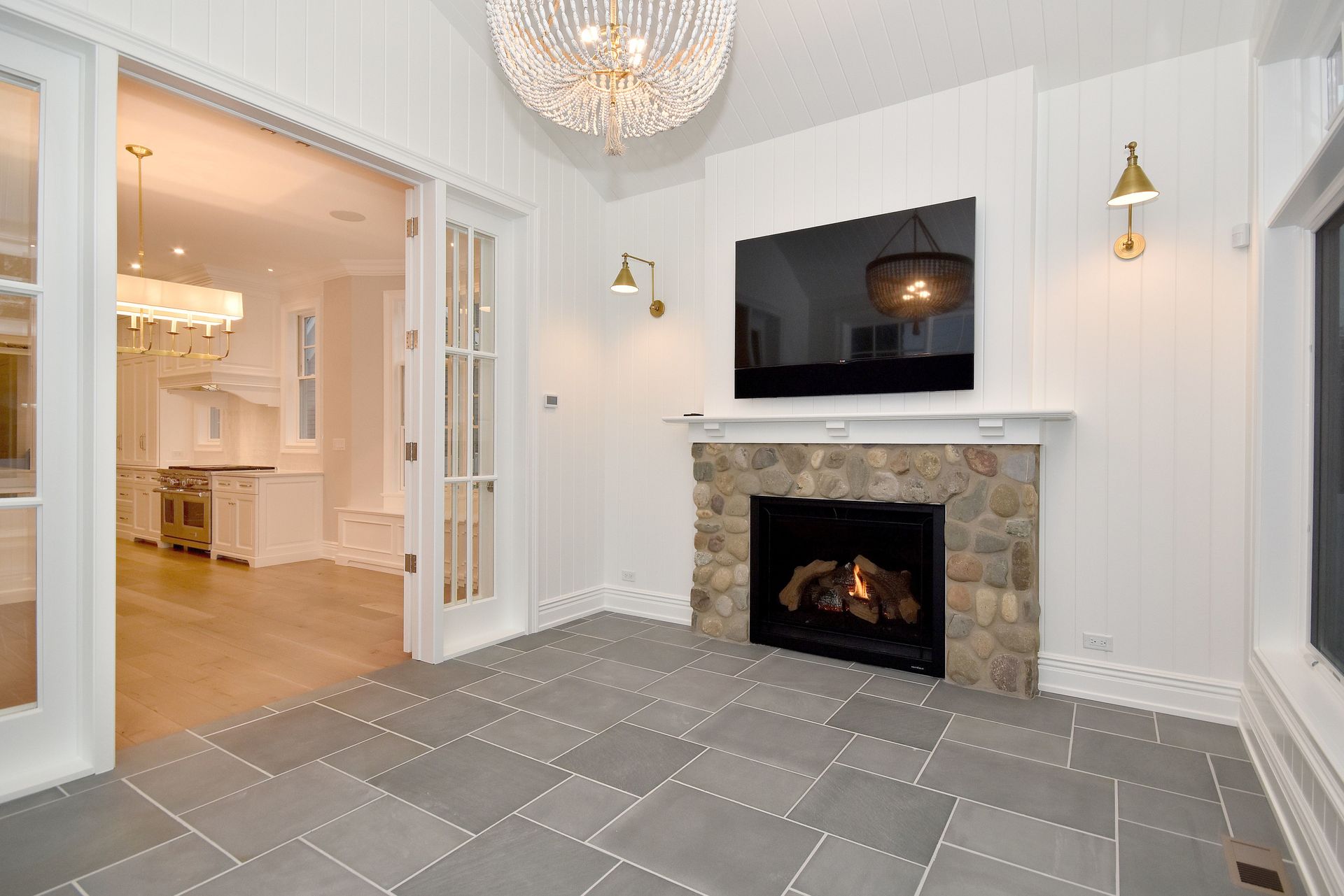 Bright living room with stone fireplace, wall-mounted TV, chandelier, and open doorway to dining area