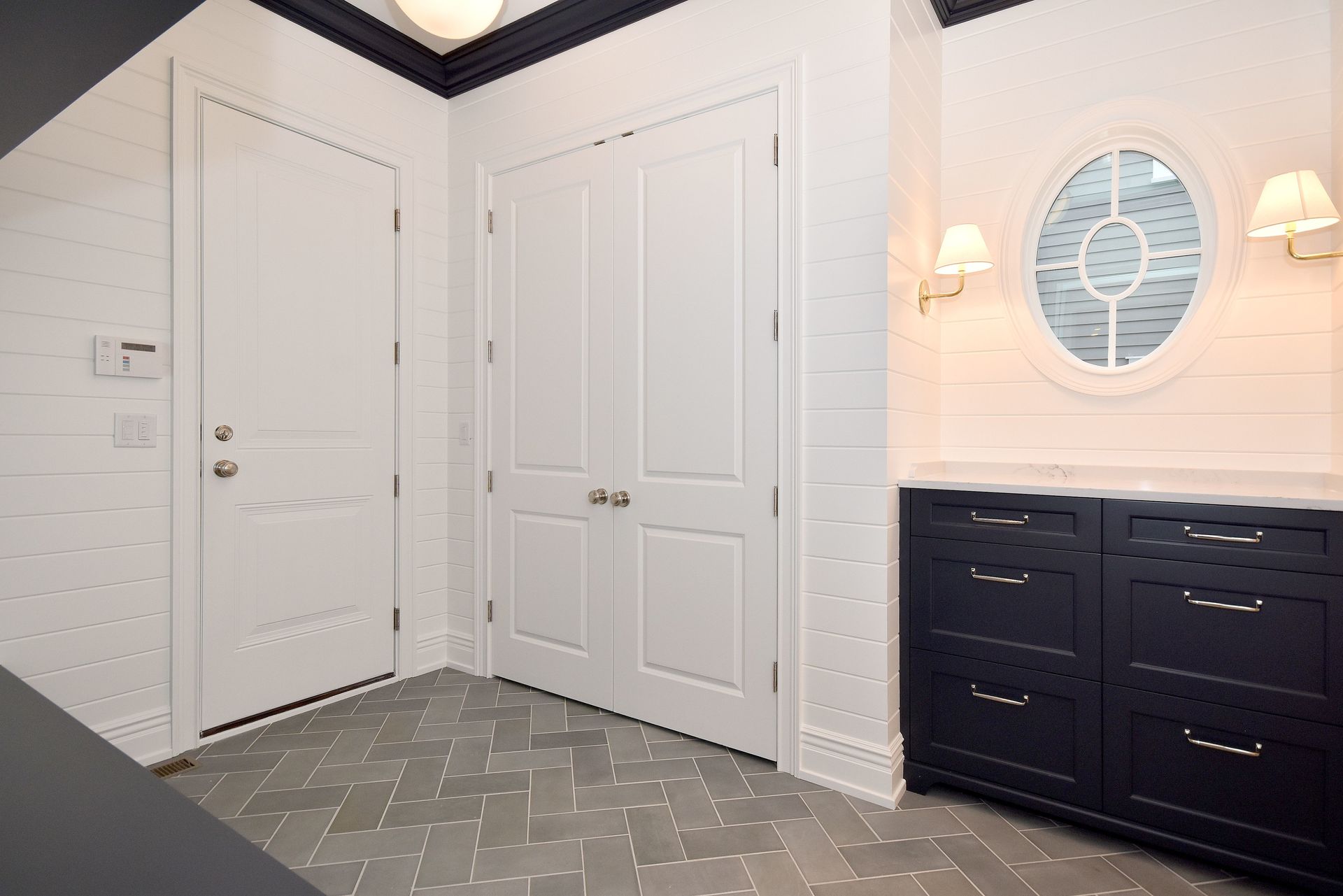 White entry hall with double doors, patterned carpet, and a dark console table beneath a round window mirror.