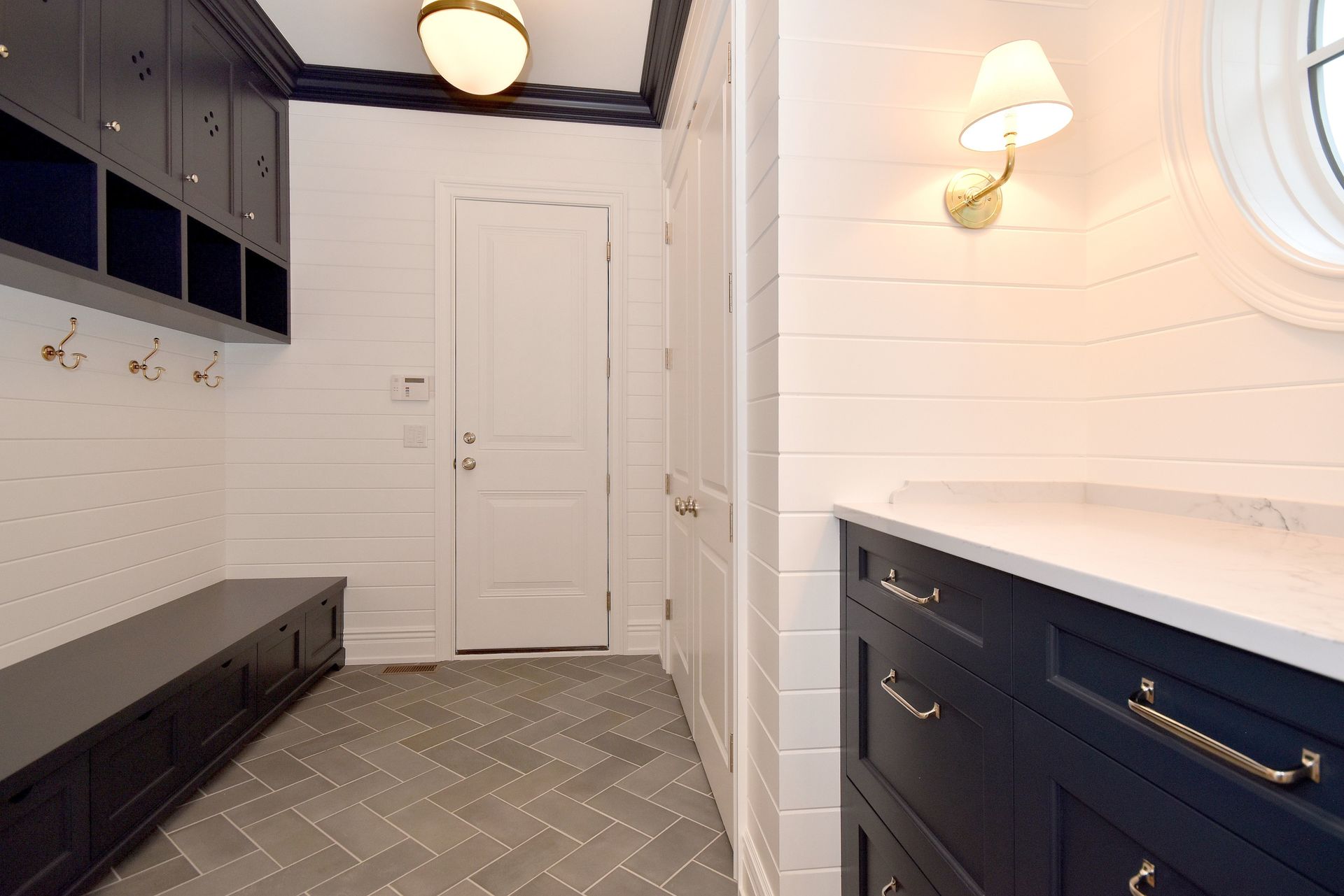 Narrow white mudroom with navy built-in cabinets, bench seating, and a patterned tile floor.