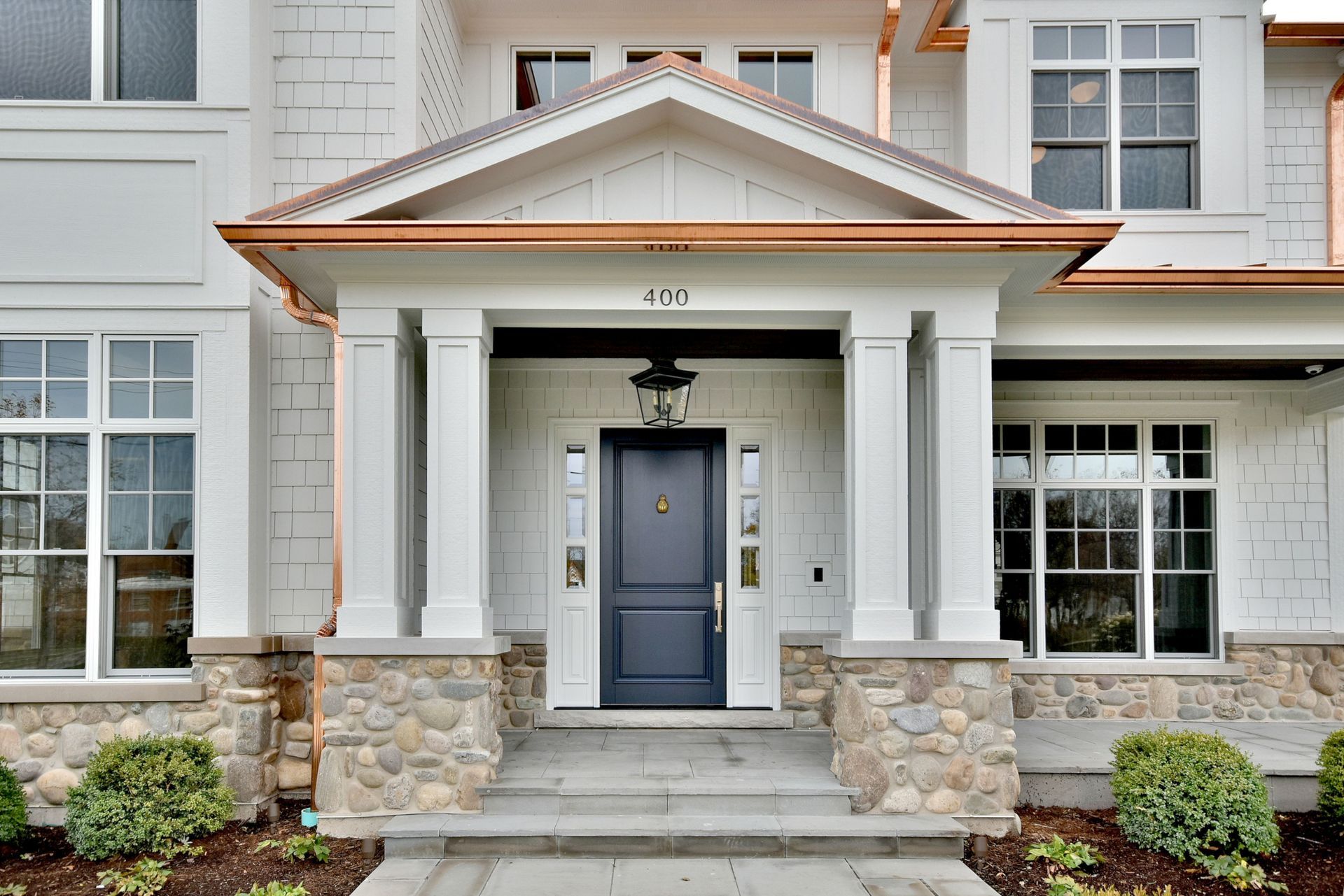 Front entrance of a white house with stone accents, blue door, and covered porch
