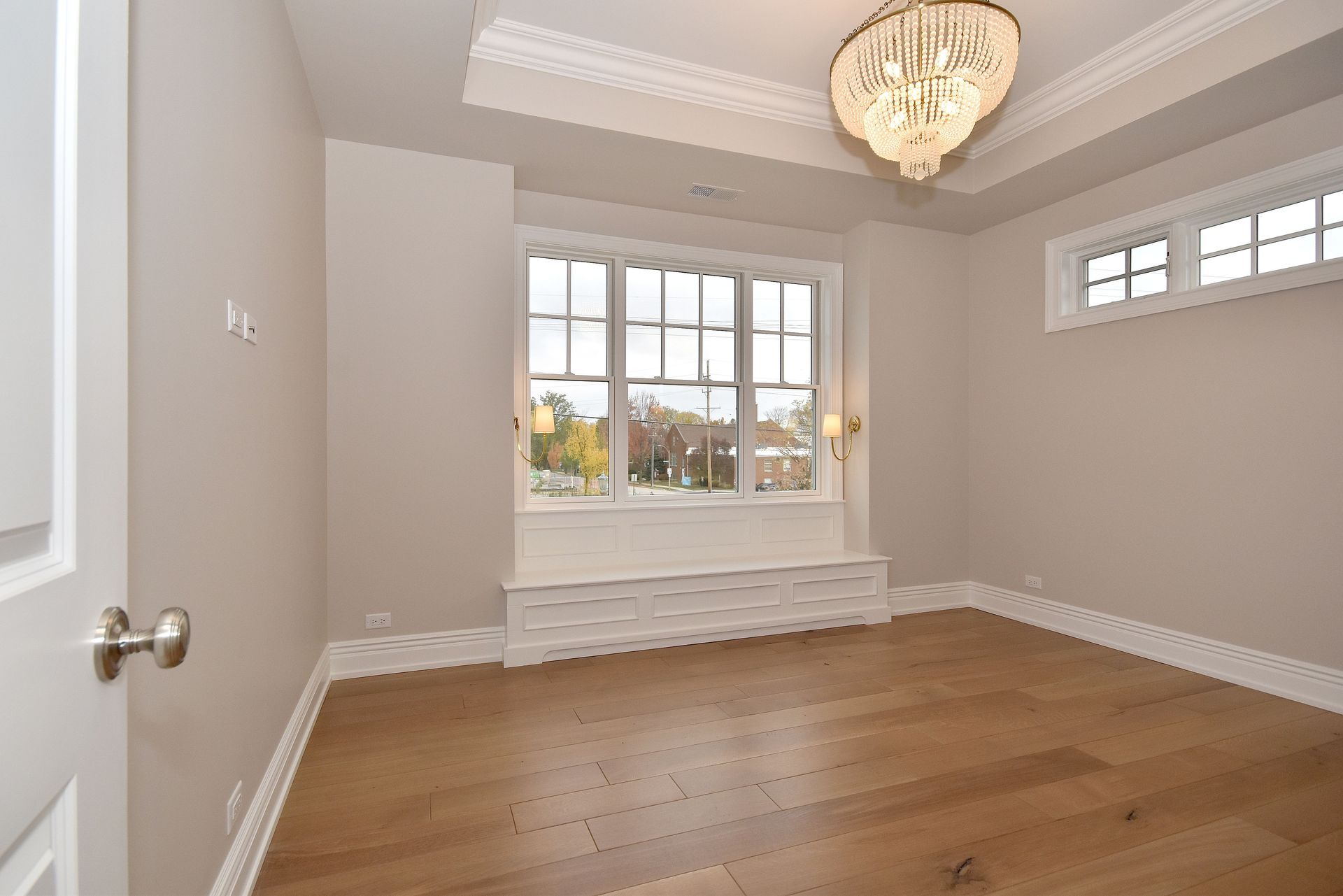 Empty beige bedroom with hardwood floors, bay window seat, and chandelier