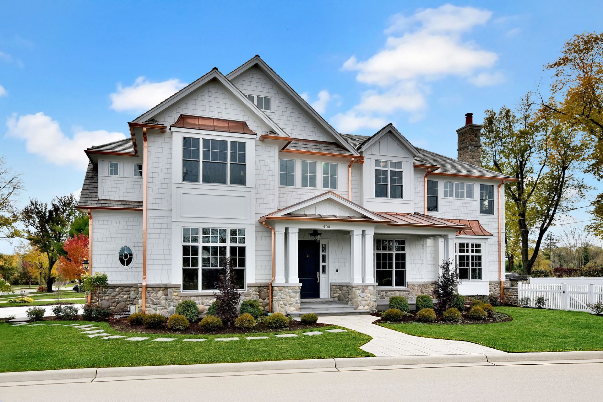 Large white two-story house with a front porch, driveway, and landscaped lawn under a blue sky
