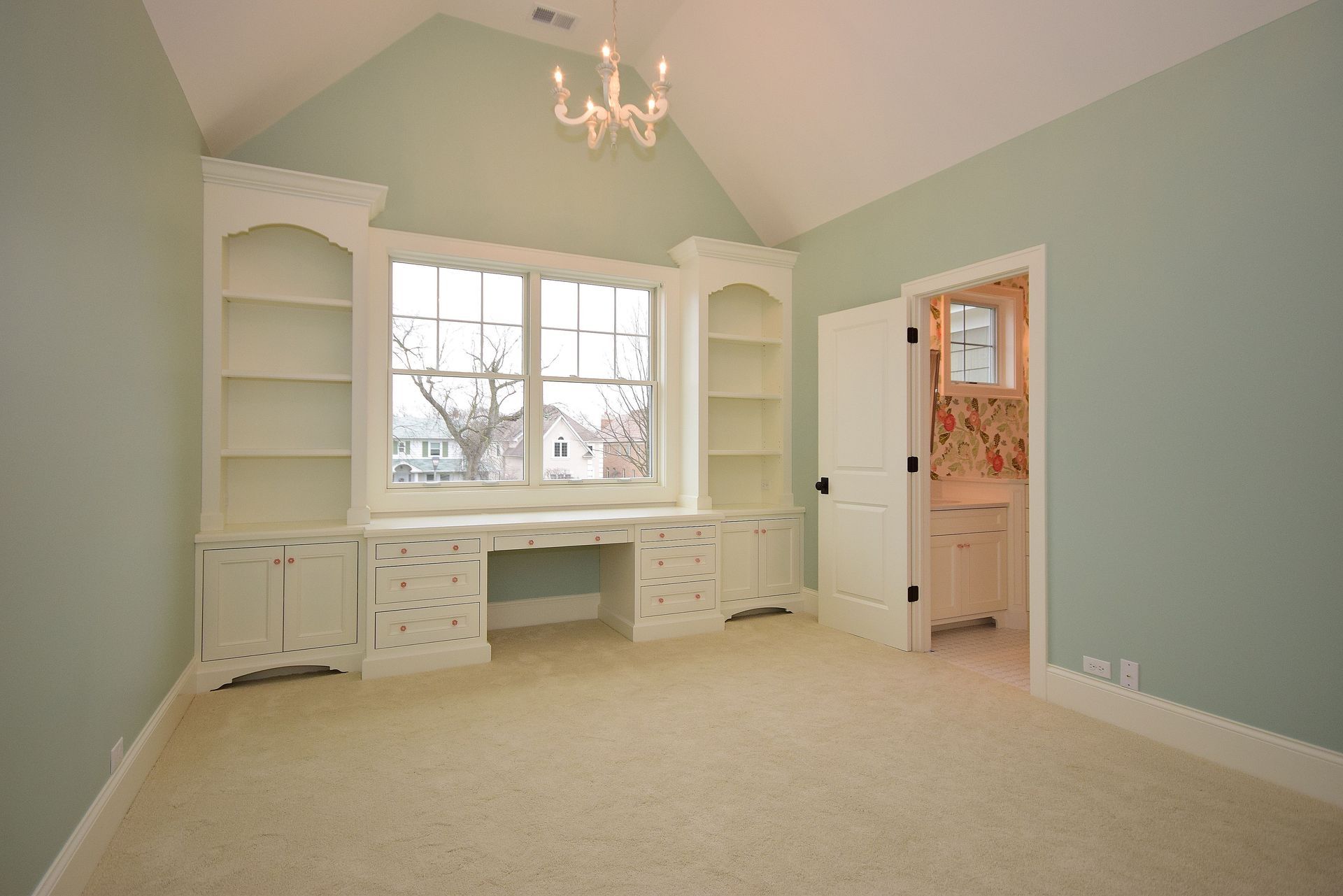 Empty pastel bedroom with built-in white desk, shelves, and a window nook.