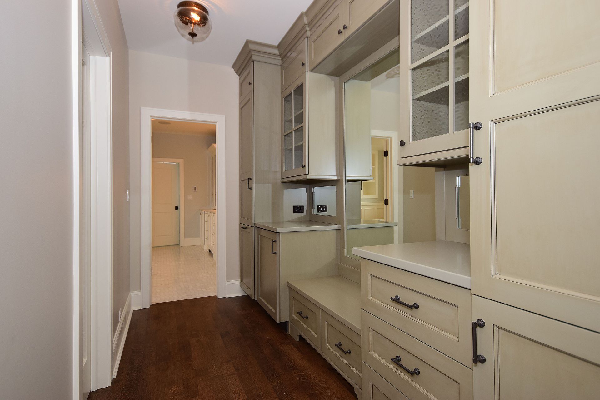 Built-in hallway cabinets with drawers and glass-front storage along a narrow white corridor with dark wood floor