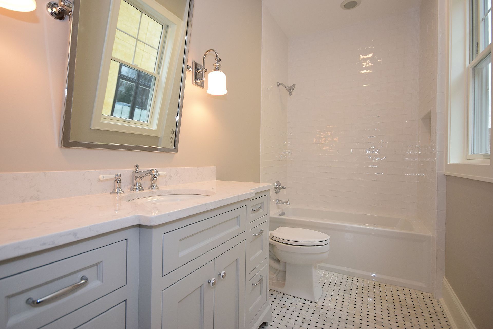 Bright modern bathroom with white vanity, mirror, toilet, bathtub, and patterned tile floor.