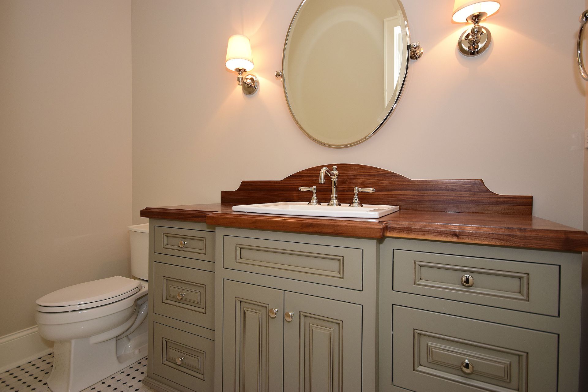 Bathroom vanity with mirror, wall sconces, and toilet in a beige and wood-toned interior