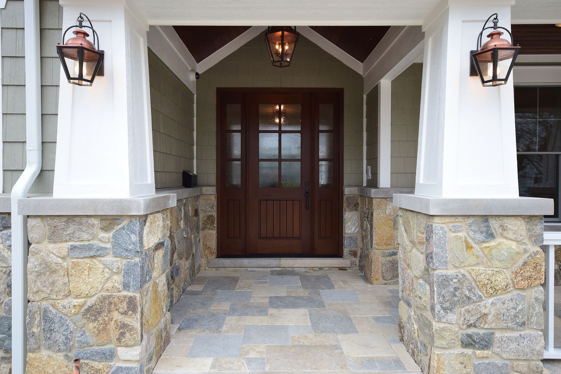 Front porch with stone columns, lanterns, and a dark wooden front door
